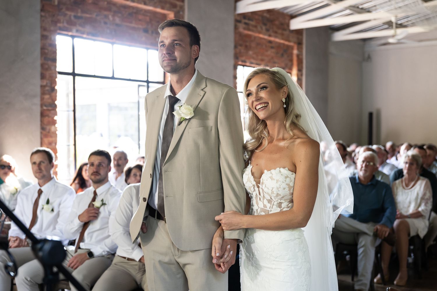 Couple stands together during wedding ceremony in modern industrial space with brick walls.