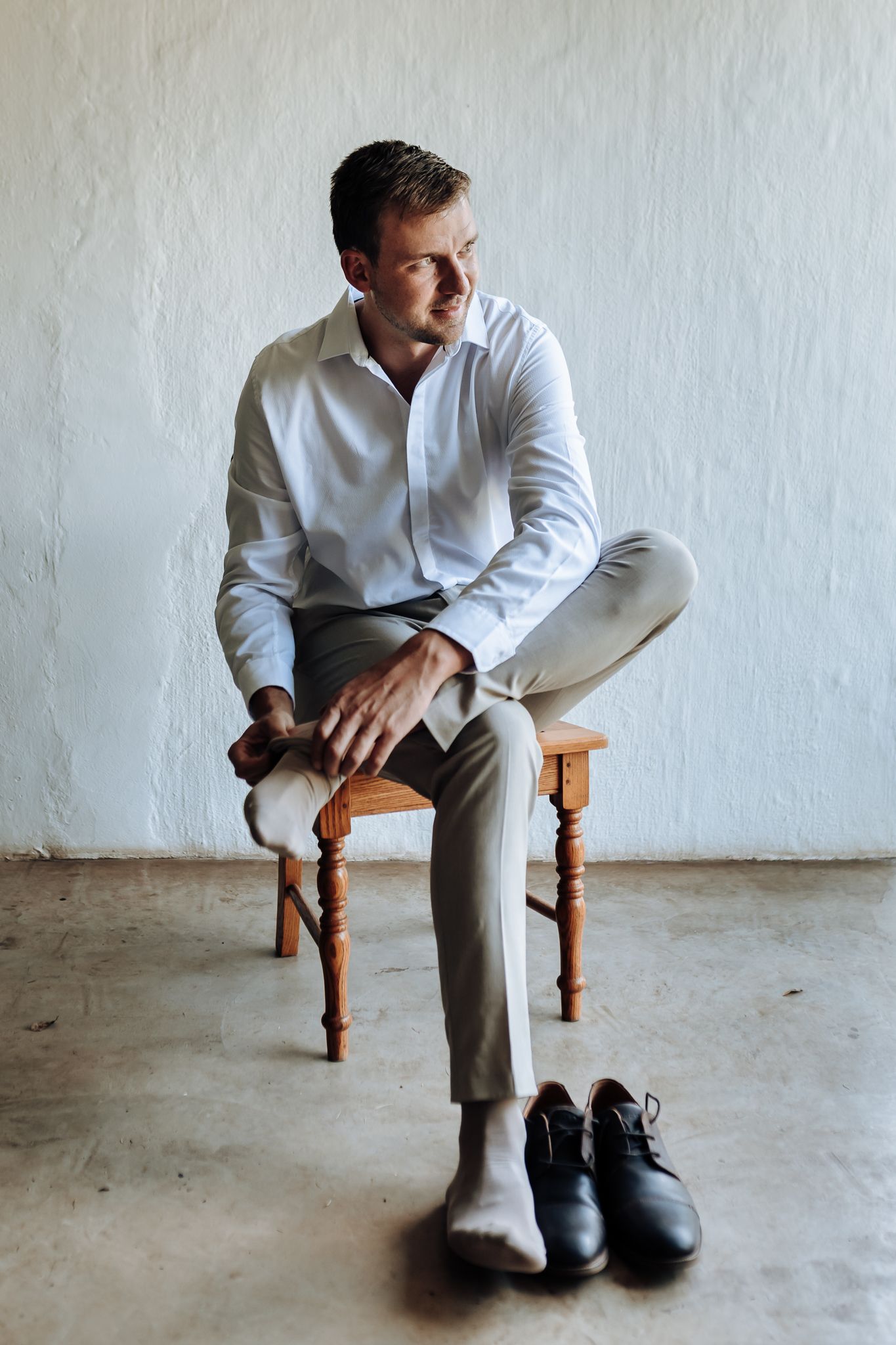 Minimalist portrait against white wall showing formal attire and dress shoes.