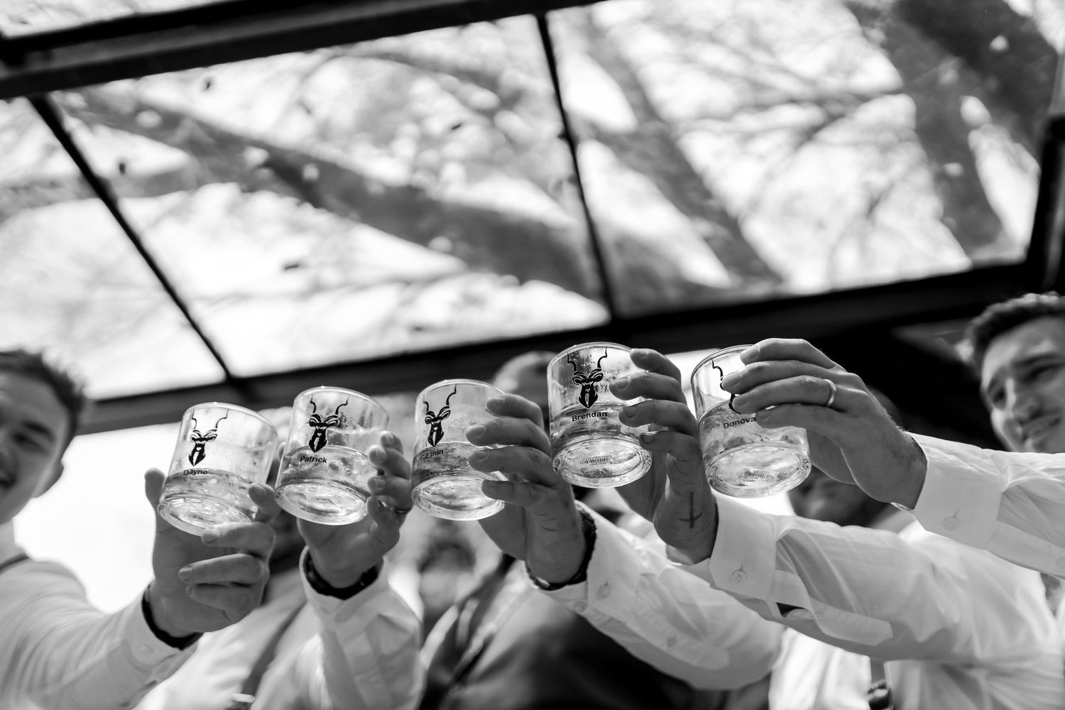 Group raising glasses in a black and white celebratory toast moment outdoors.