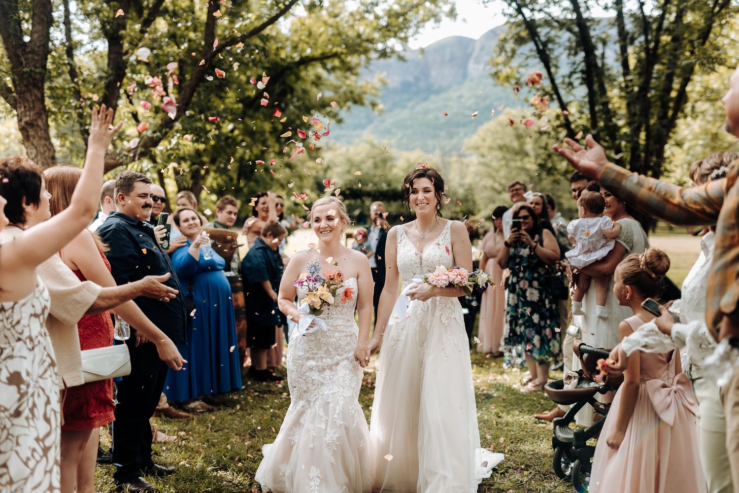Joyful wedding celebration with guests throwing confetti in a wooded outdoor venue.