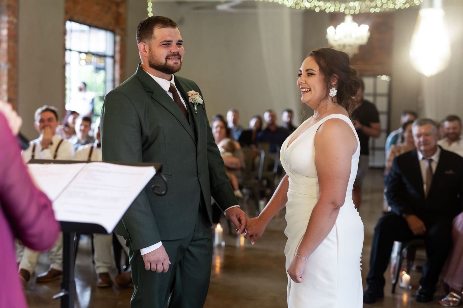 A joyful wedding ceremony moment captured in a venue decorated with string lights and chandeliers.
