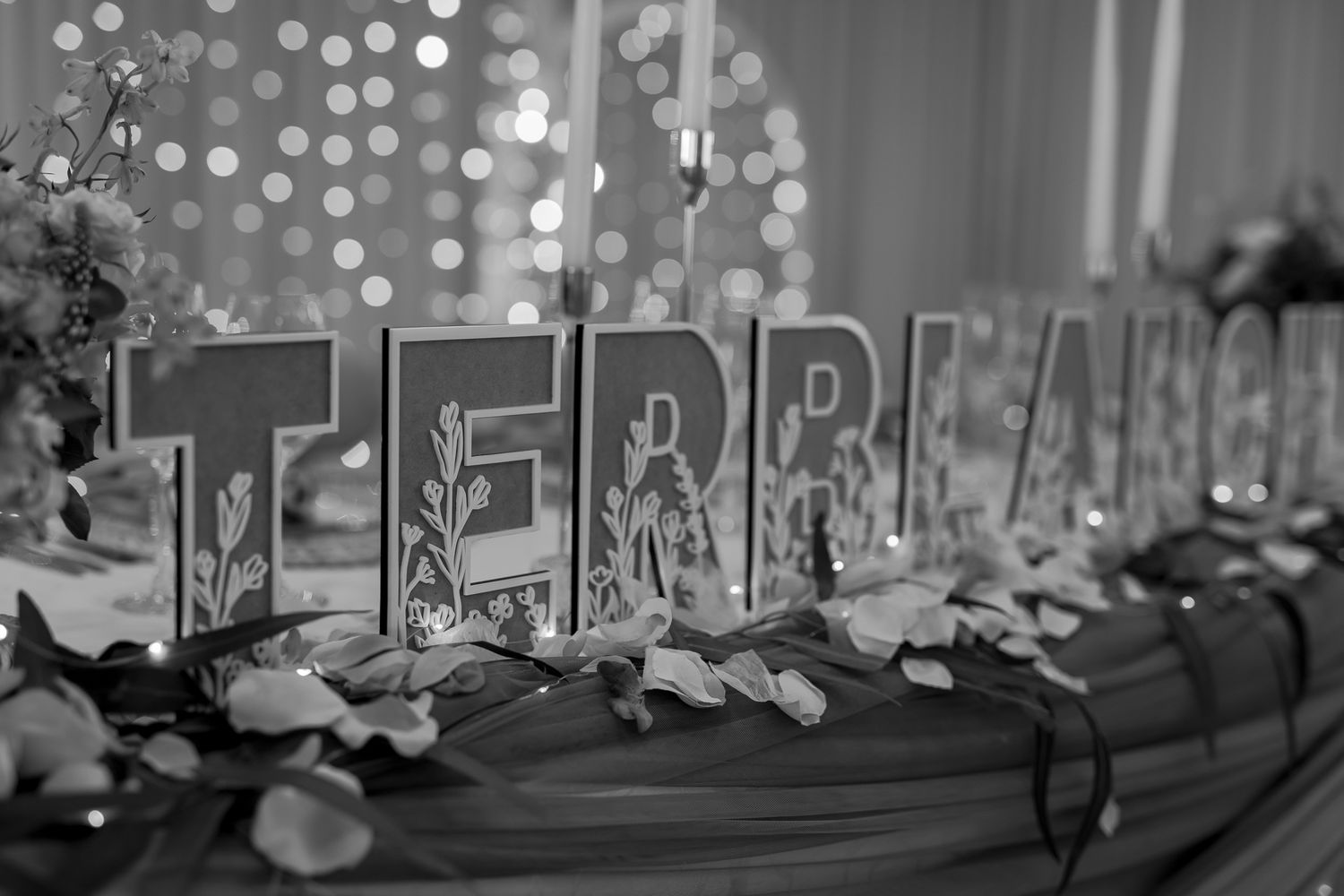 Black and white image of wedding decor spelling out 'Team' with bokeh lights in background.
