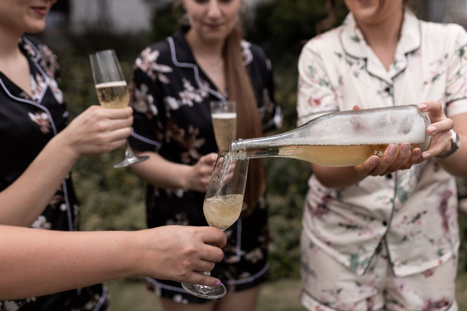 Hands pour champagne into glasses during outdoor celebration.