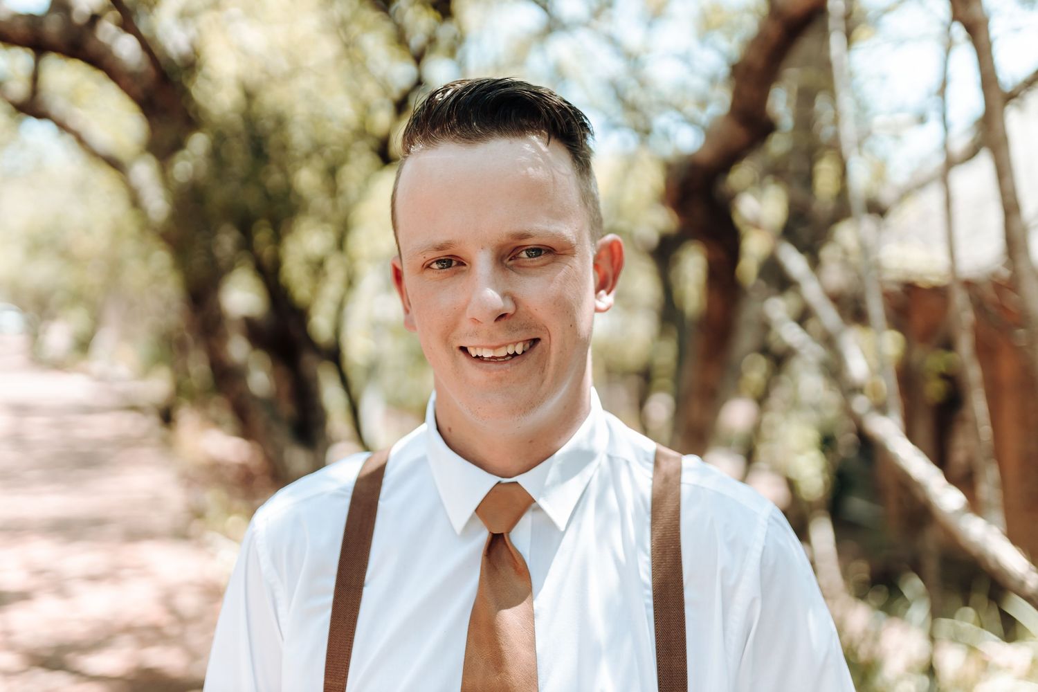Outdoor portrait showing formal attire with white shirt, brown tie and leather suspenders.