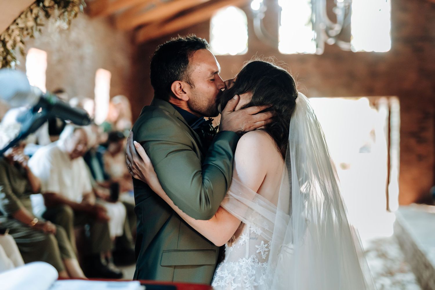 Newlyweds embrace and kiss under an archway during their wedding ceremony.