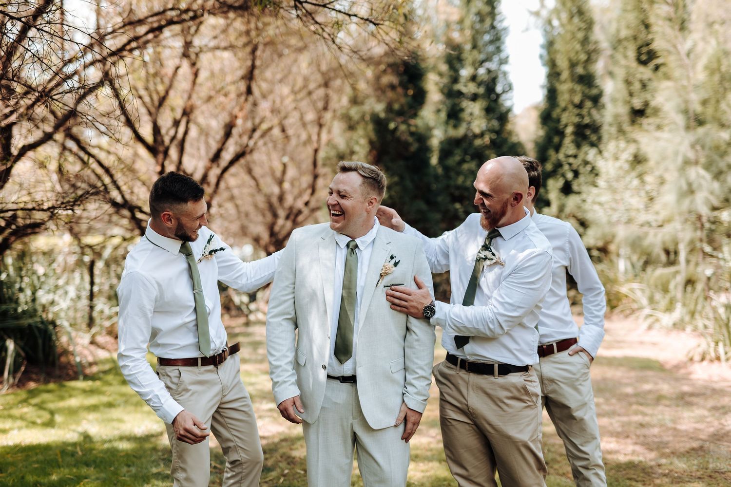 Wedding party shares candid moment while walking together outdoors in light formal wear.
