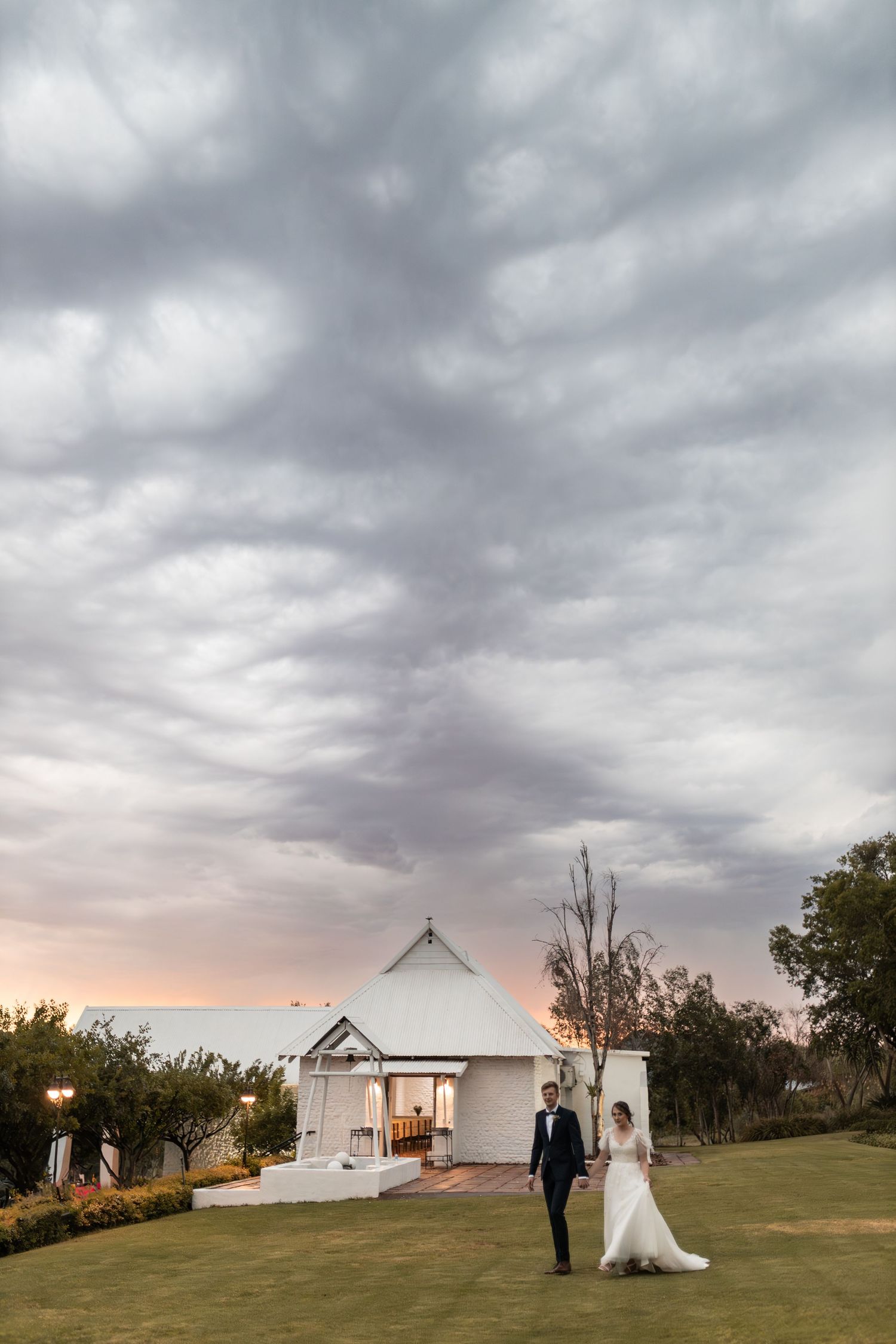Wedding photograph with dramatic cloudy sky above white chapel venue at sunset.