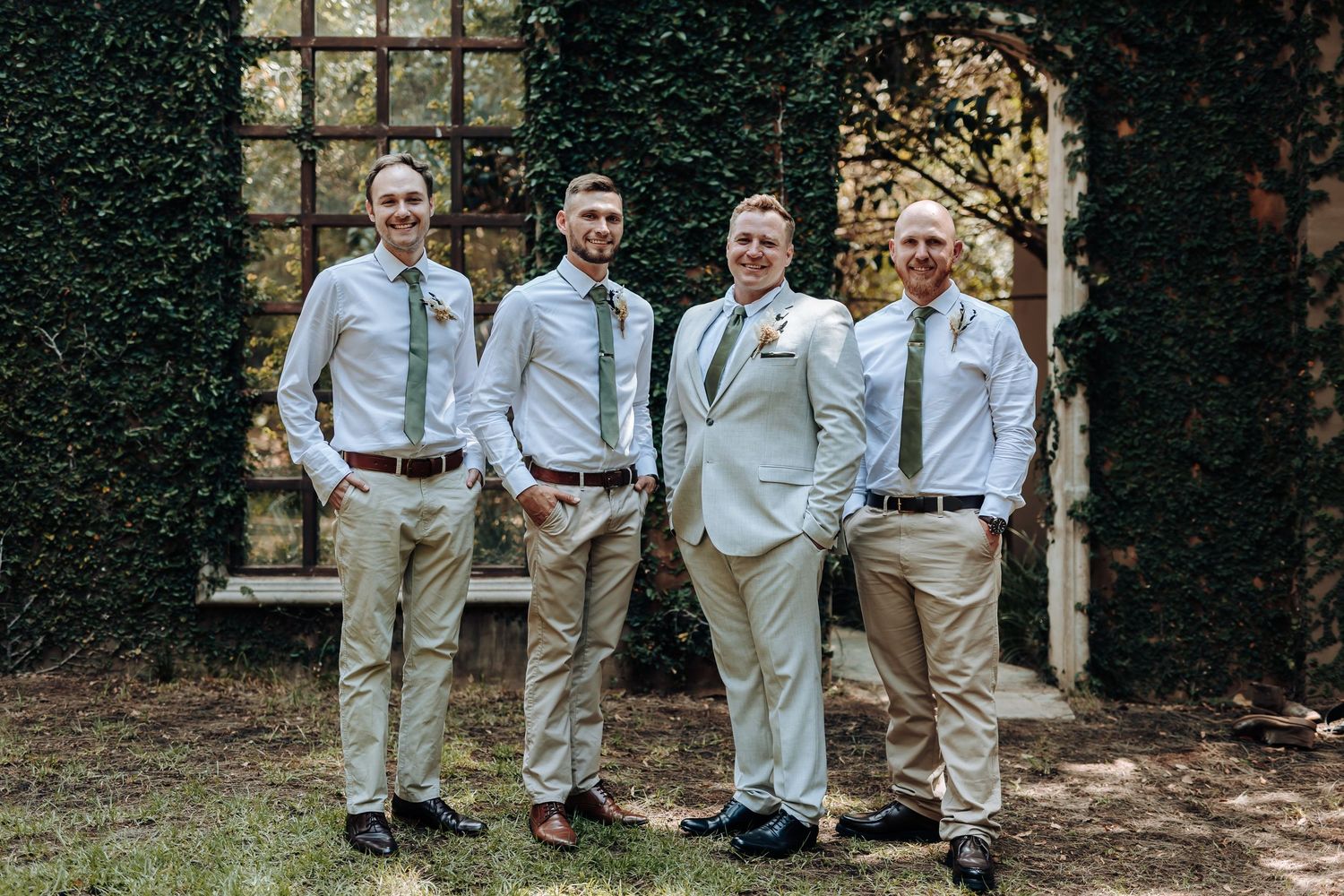 Groomsmen and groom in coordinating light outfits stand together for casual wedding photo.