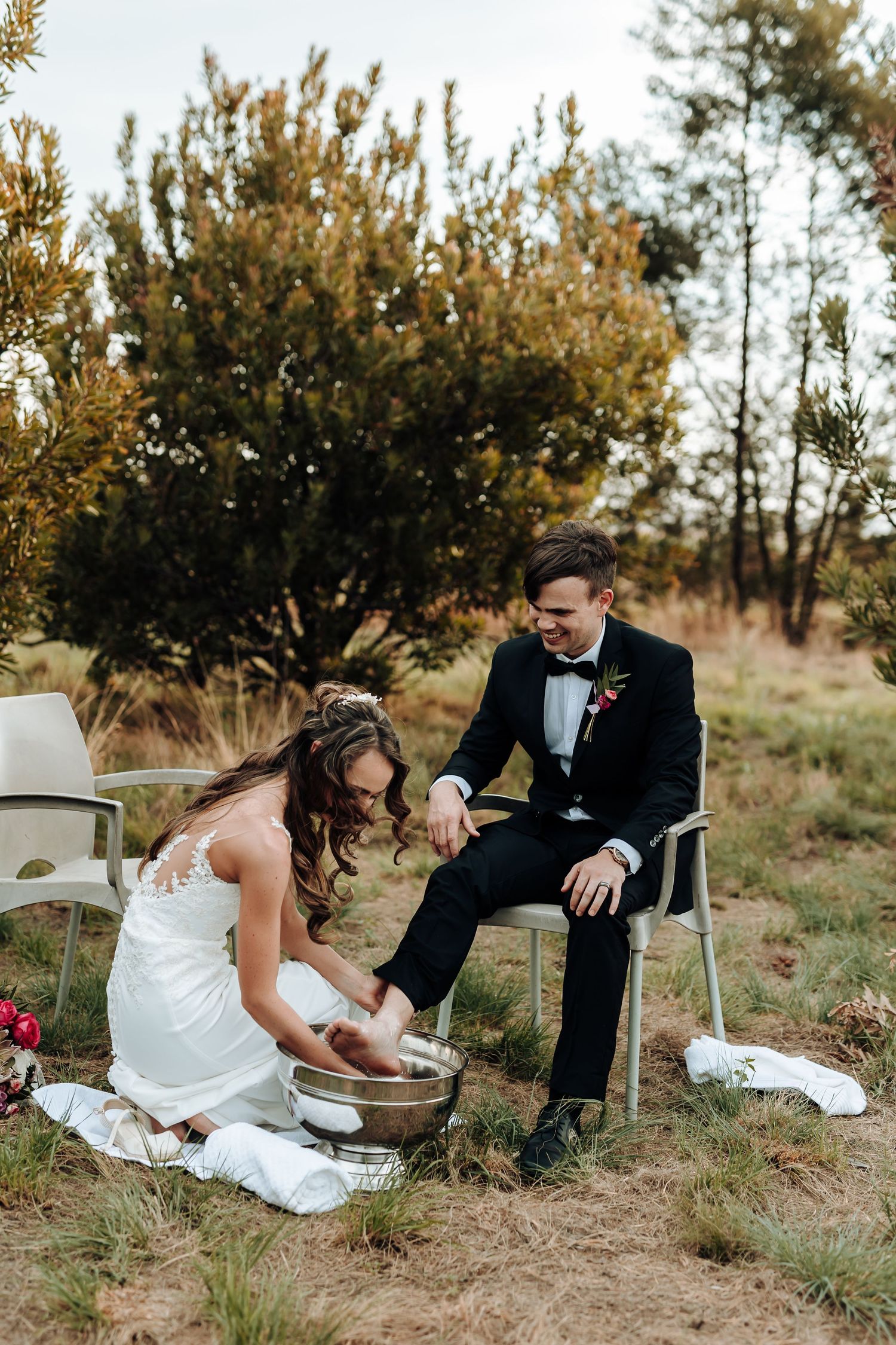 Wedding couple participates in foot washing ceremony outdoors with rustic decor.