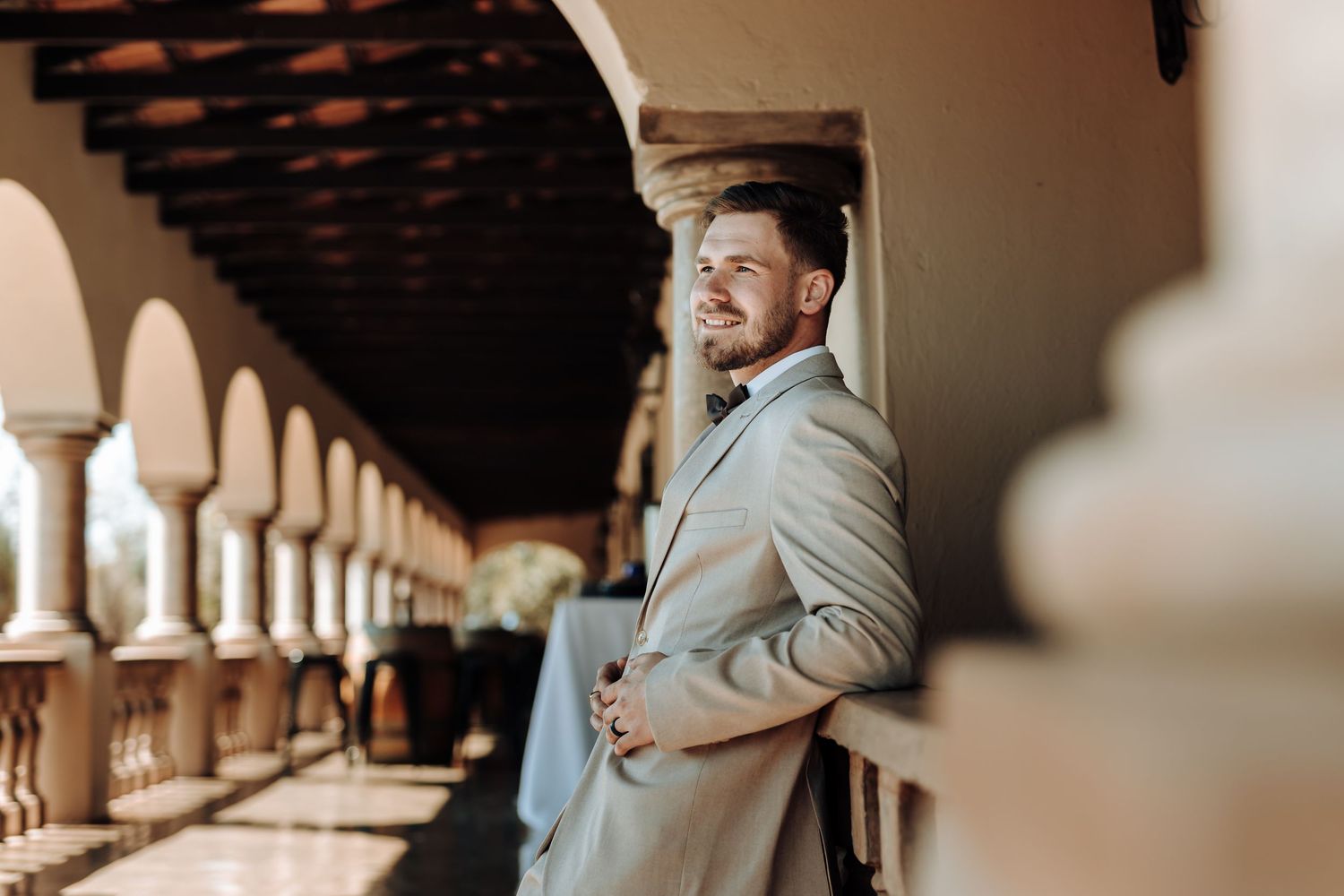 Side view portrait of someone in a light suit posing along a columned walkway.