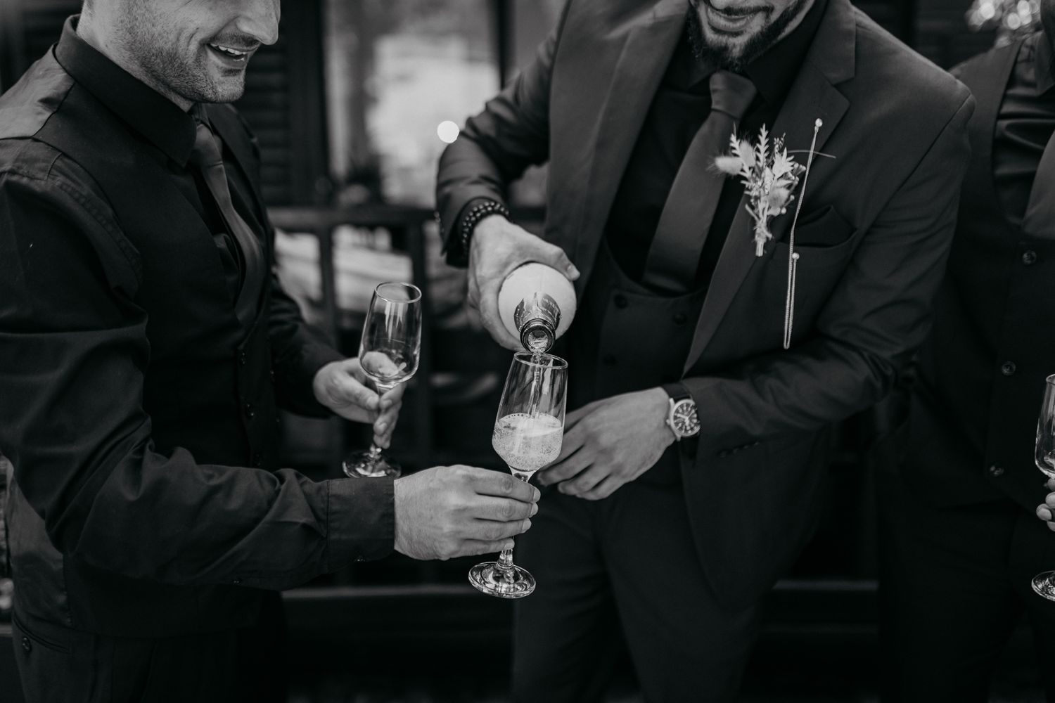 Close-up of hands pouring champagne into glasses in black and white.