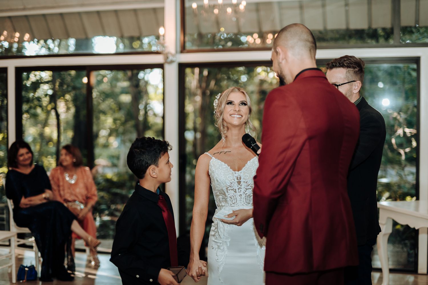 Wedding ceremony taking place in a bright indoor venue with chandelier lighting.