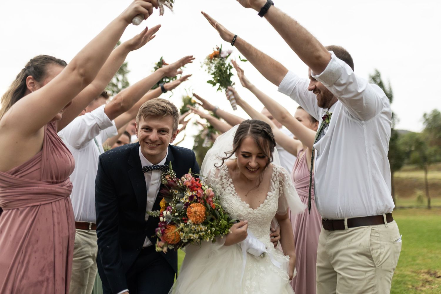 Wedding party creates a tunnel of raised arms for couple to walk through outdoors.