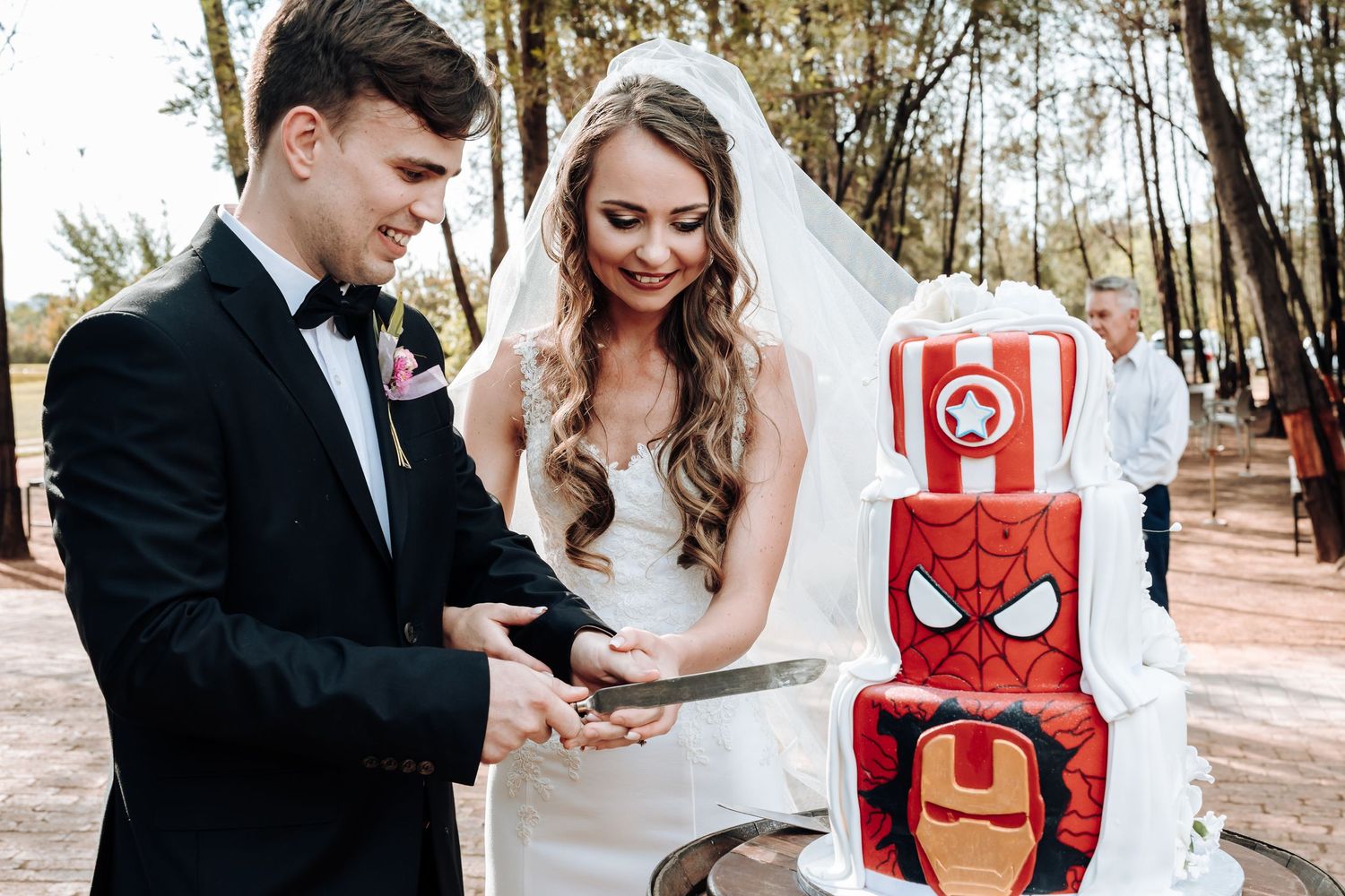 Couple admiring their Marvel superhero-themed wedding cake displayed outdoors.