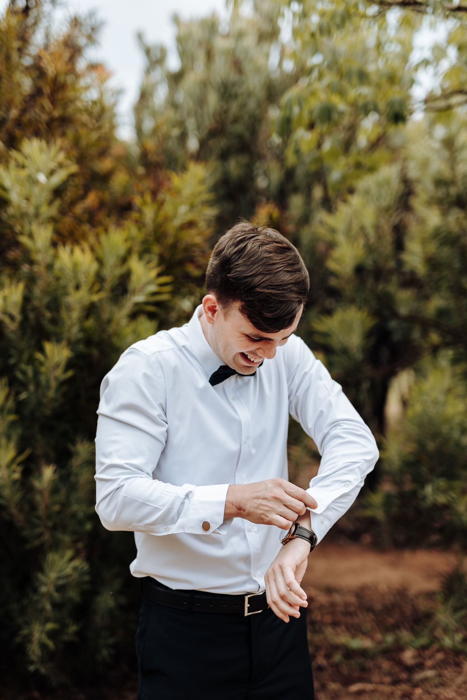 Someone in white dress shirt adjusting cuff links outdoors.