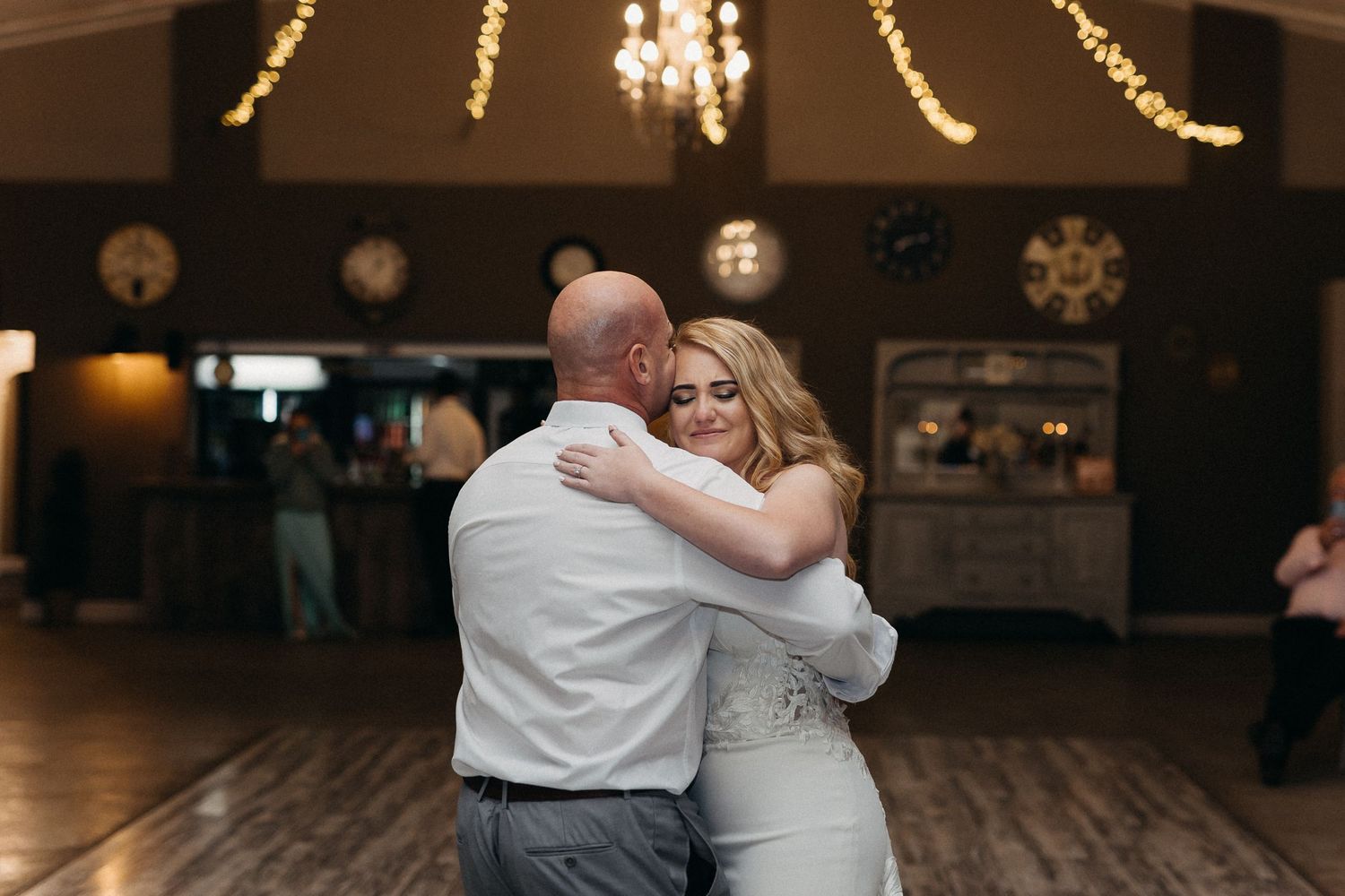 Couple sharing an intimate slow dance moment on wooden dance floor with string lights overhead.