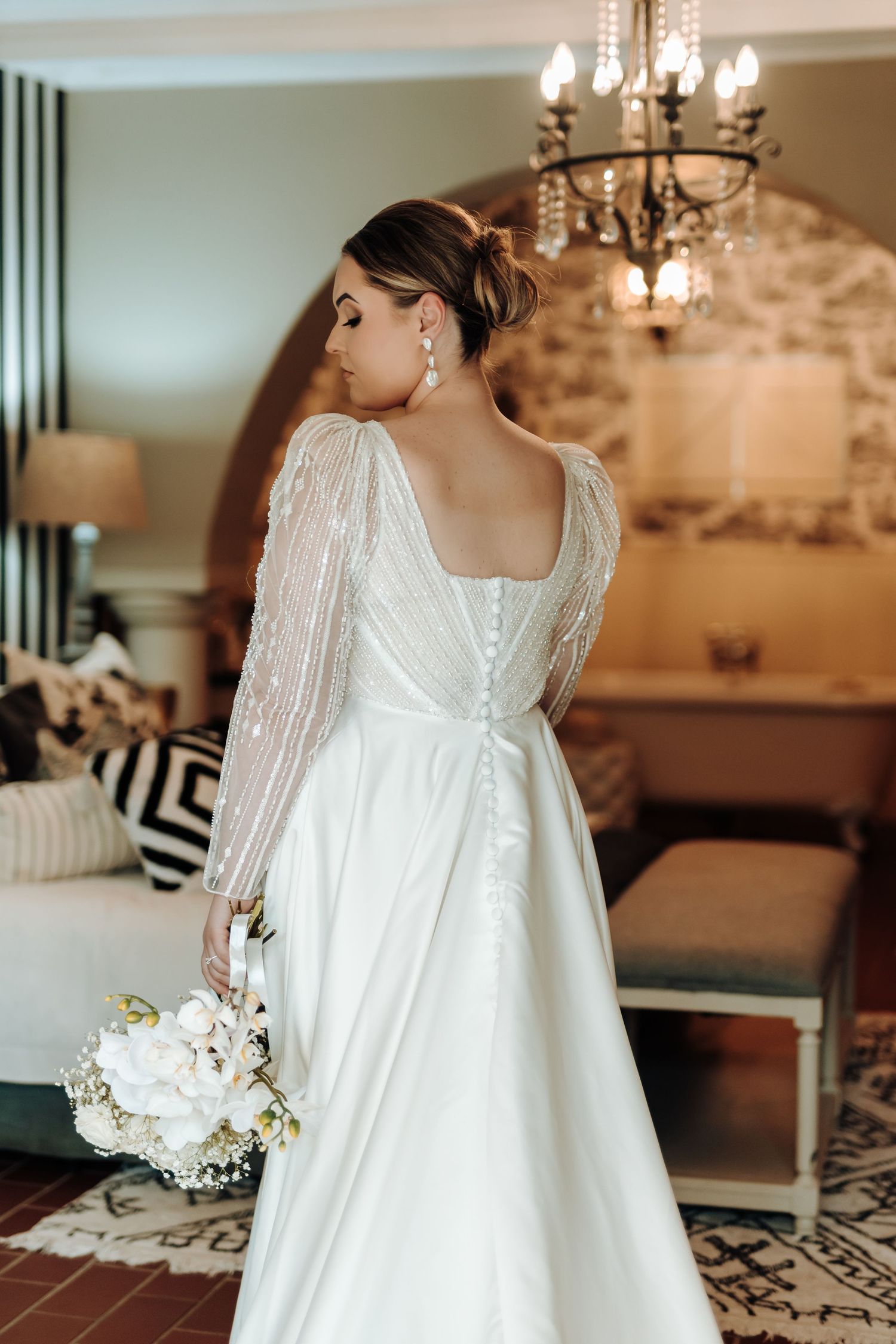 Detailed back view of wedding dress with buttons and flowing train holding white bouquet.