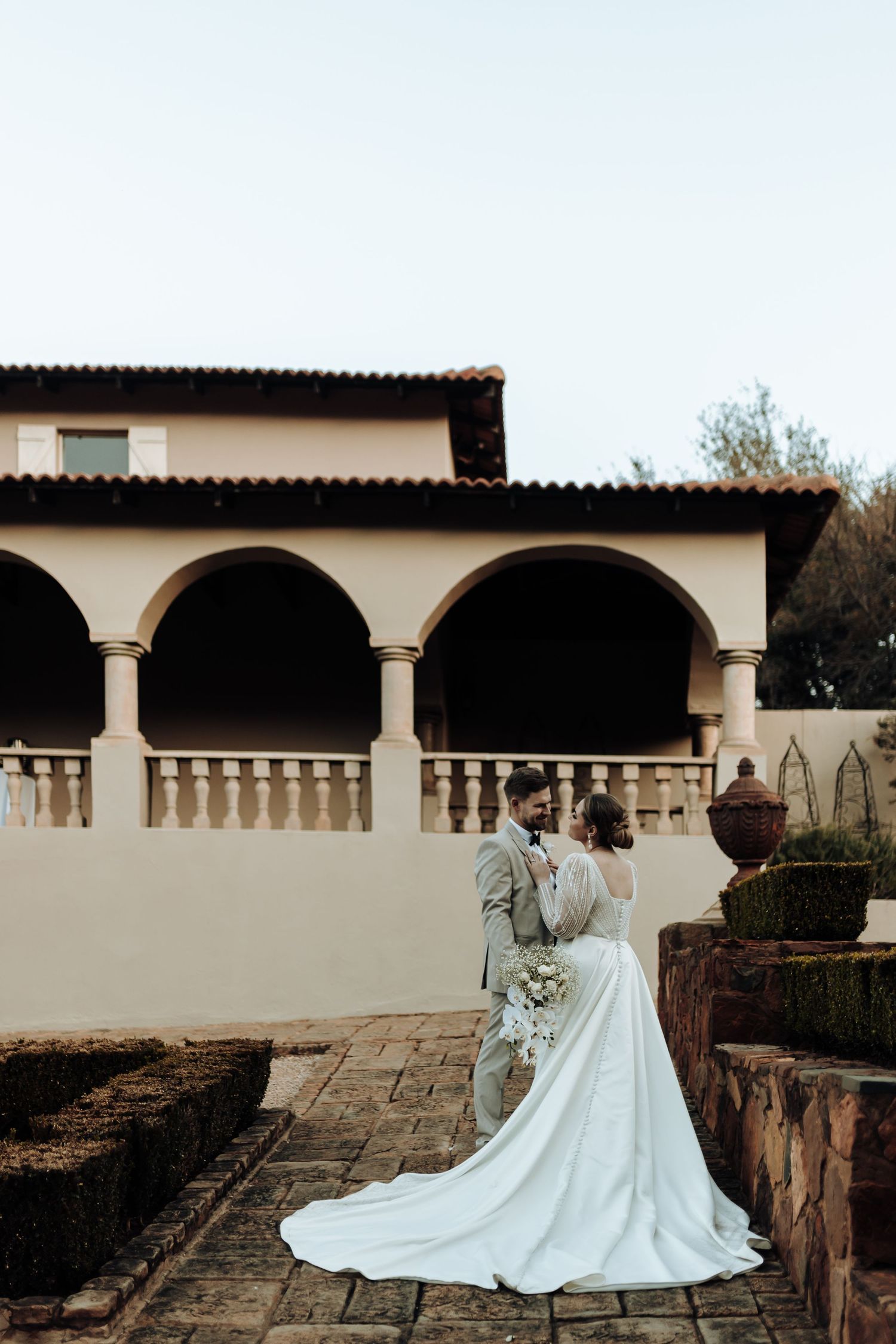 Wedding couple photographed against stone terrace and Spanish colonial architecture.