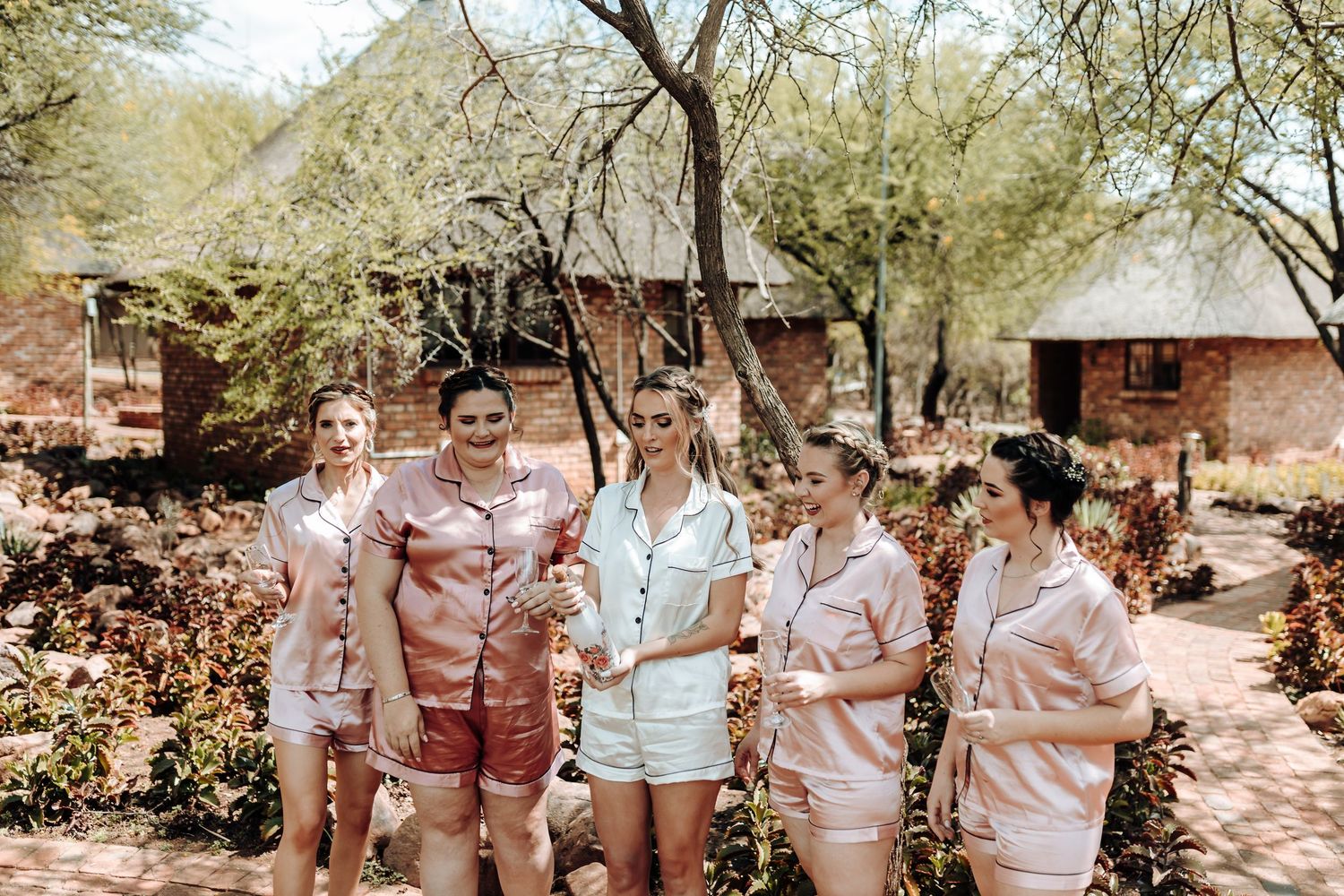 Group wearing coordinated pink and white satin pajama sets standing together outdoors.