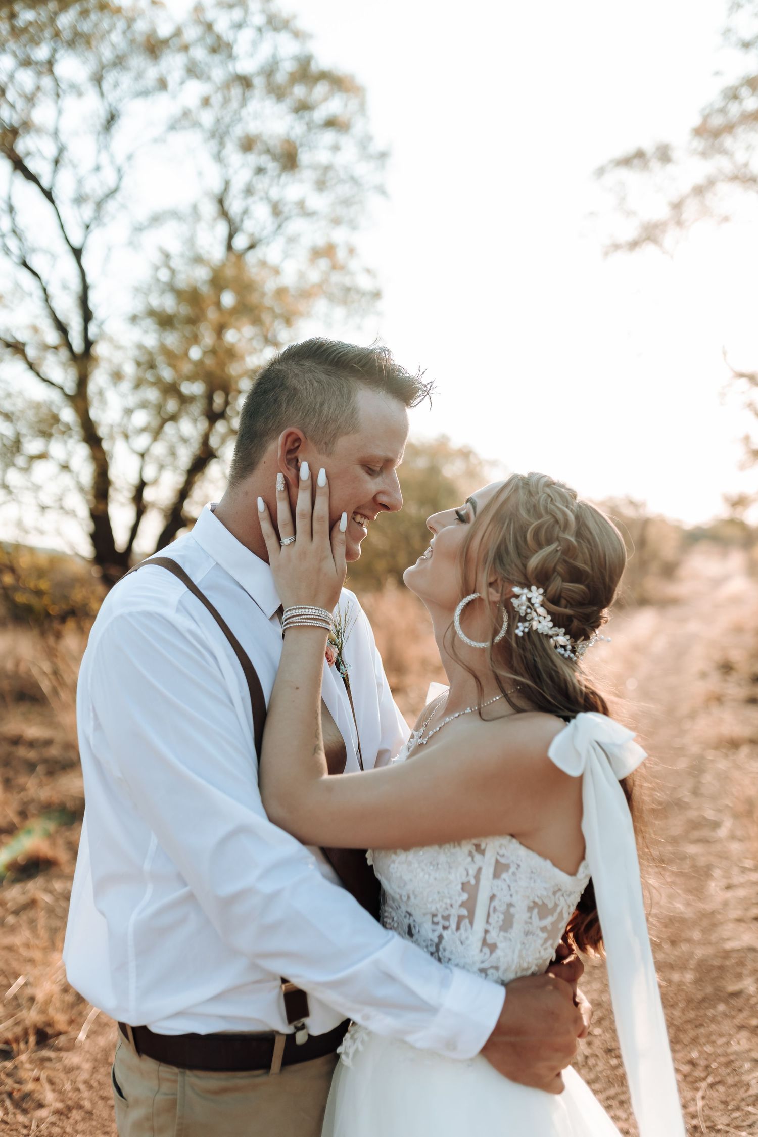 Intimate wedding couple embraces in golden field at sunset with romantic lighting and natural backdrop.
