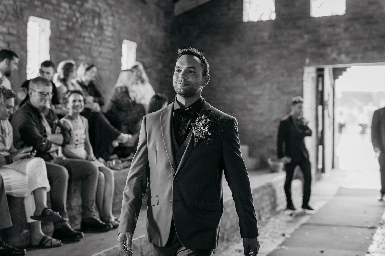 Person in formal suit standing in rustic brick venue during wedding ceremony.