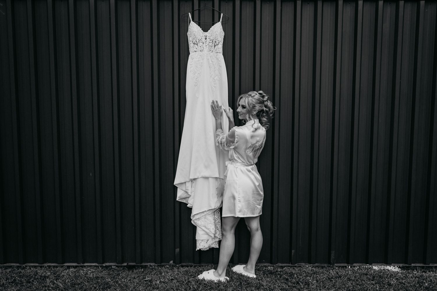 Black and white photo of wedding dress preparation against dark wall.