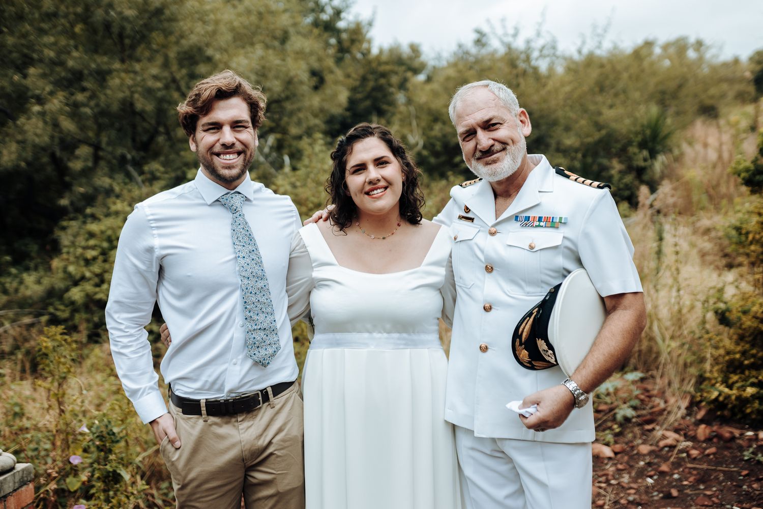 Wedding party members smile together in outdoor garden setting.