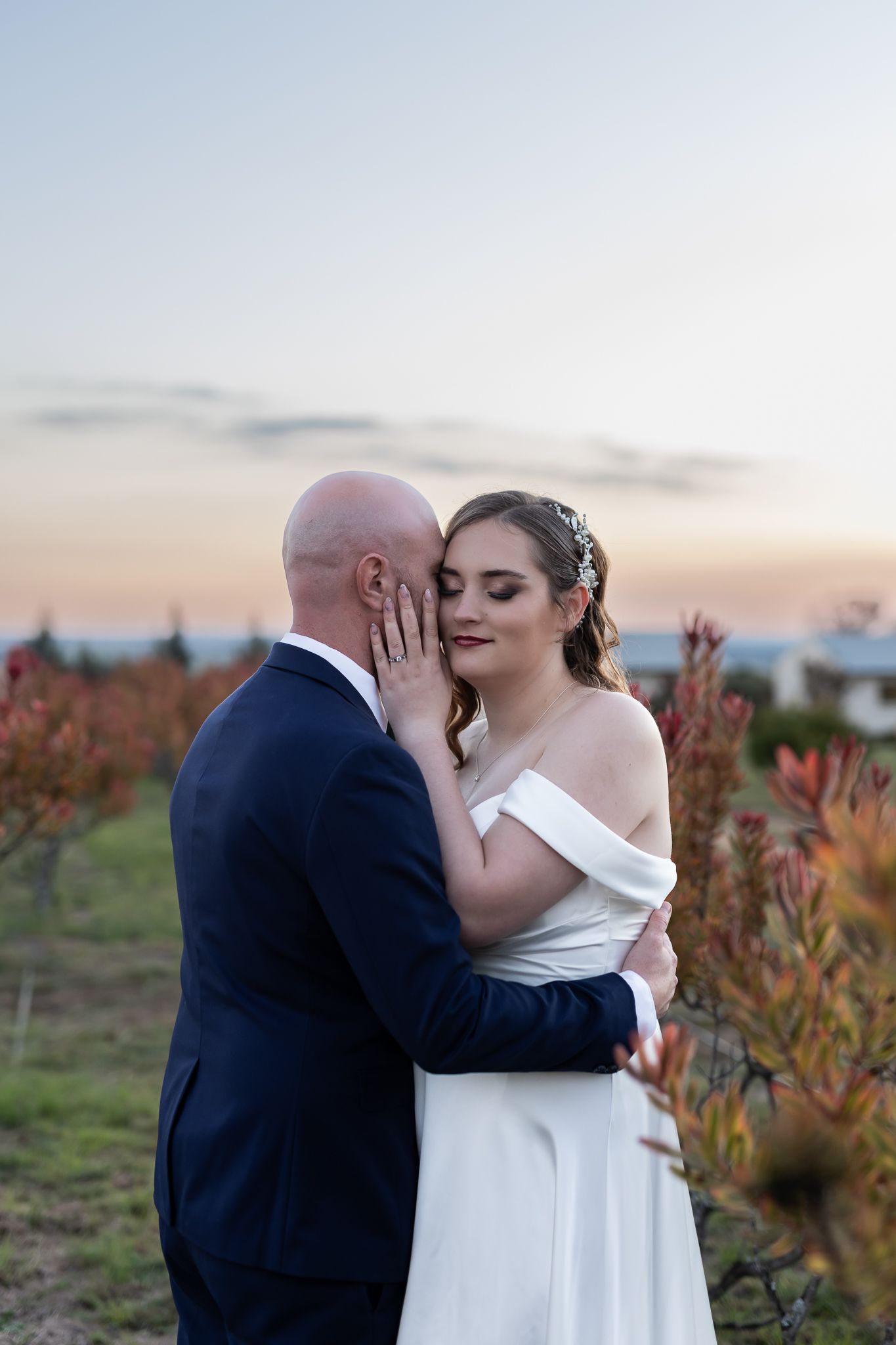 Intimate moment between newlyweds during sunset in a garden setting.