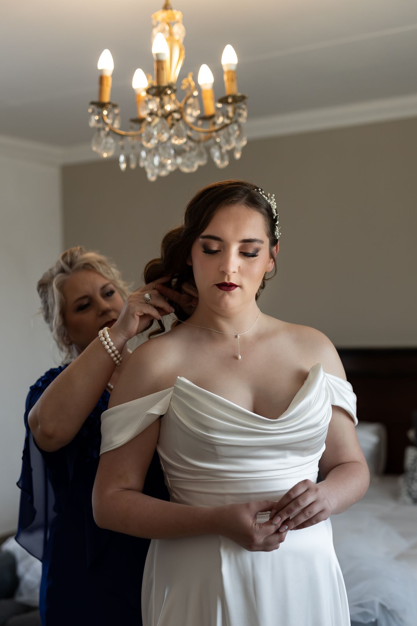 Final wedding dress adjustments being made in an elegant bedroom setting.
