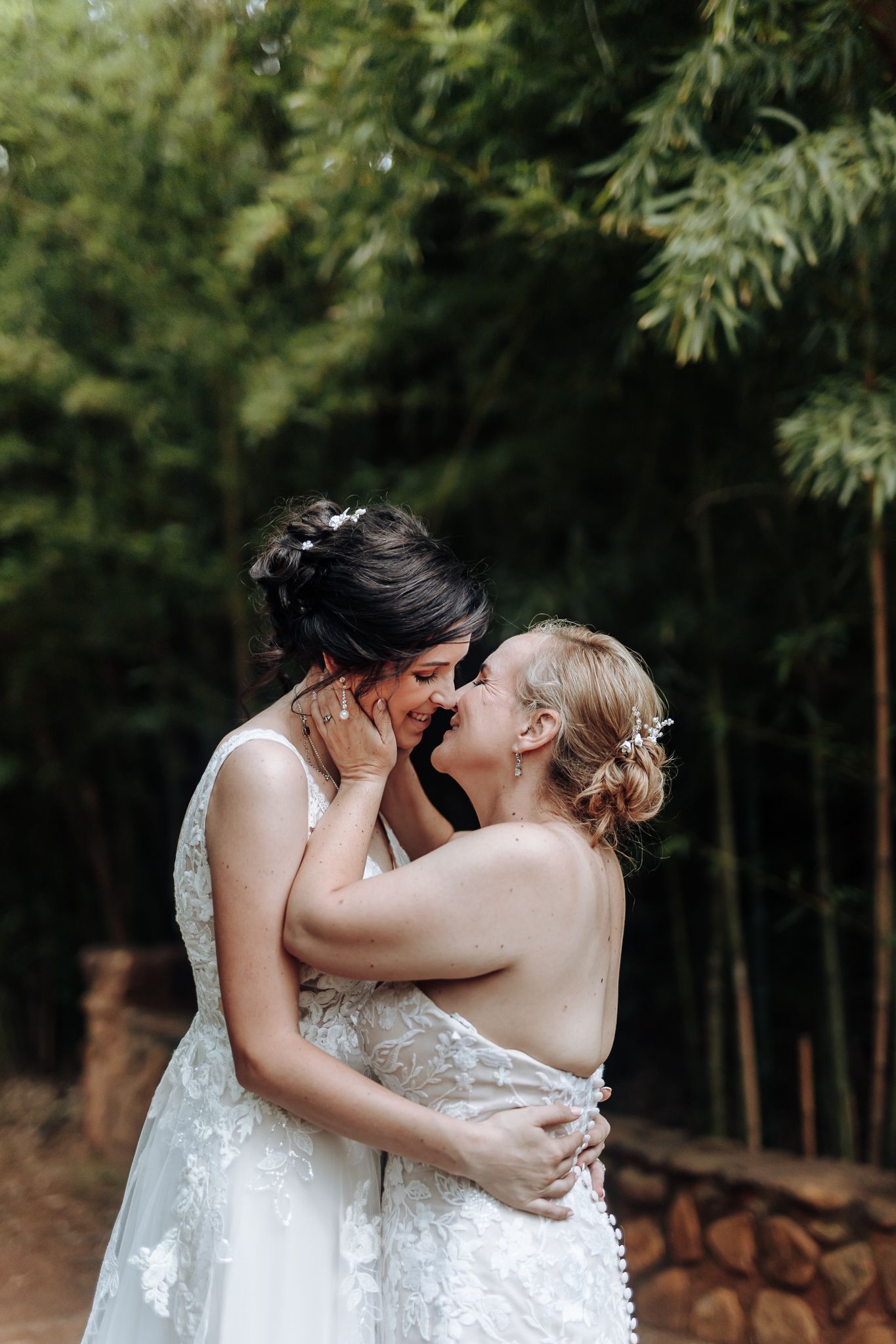 Two people in elegant white wedding dresses against a bamboo forest backdrop.