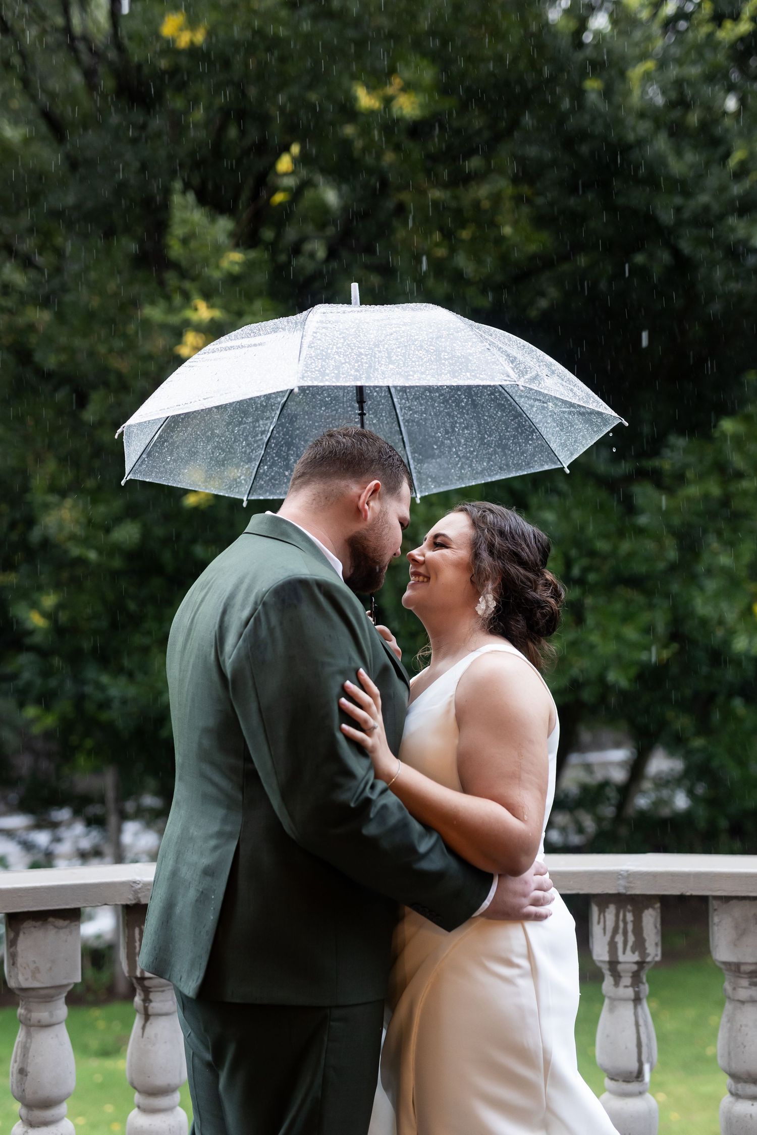Couple shares joyful moment under clear umbrella on outdoor stone balcony.