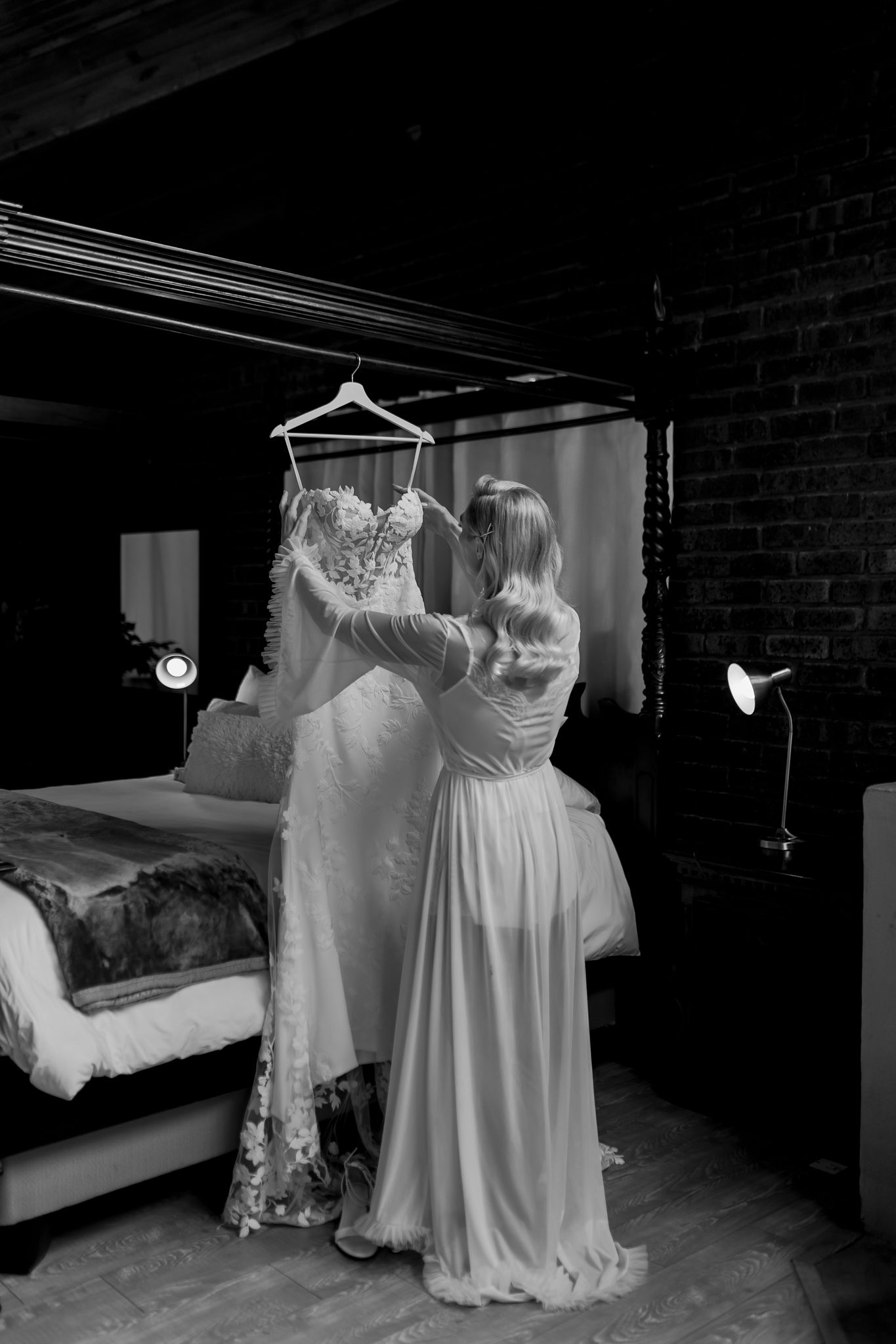 Wedding dress being adjusted in moody black and white setting with exposed brick wall.