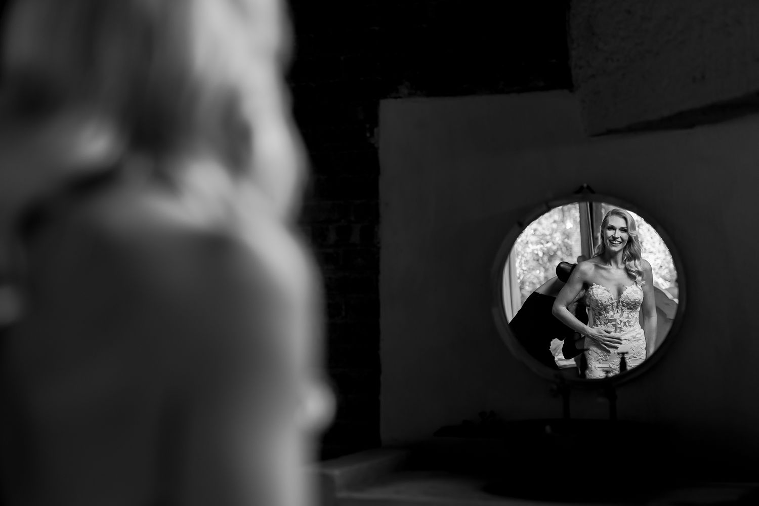 An artistic black and white reflection of a bride in a circular mirror.