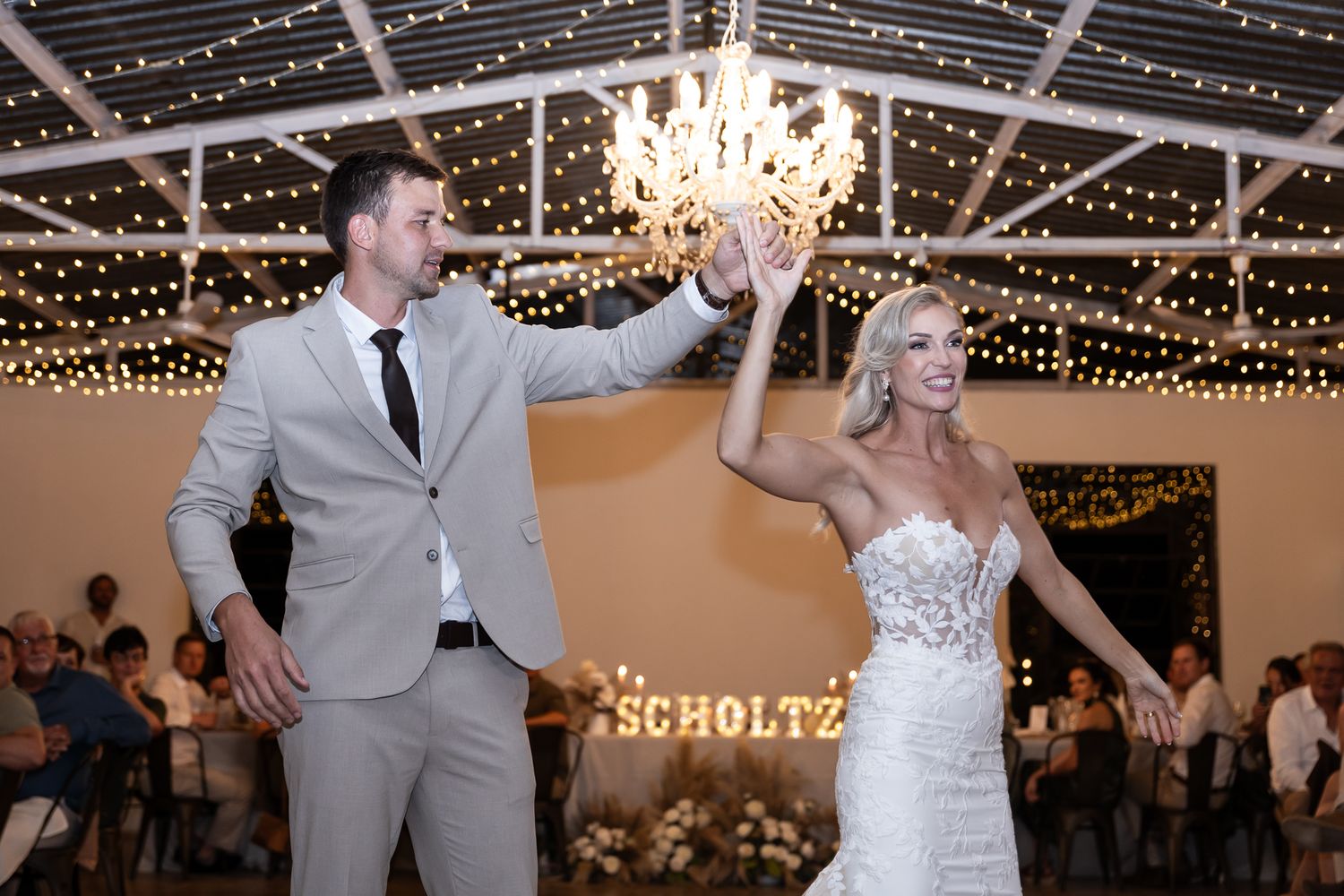 Joyful wedding couple dancing under sparkling lights and chandelier at reception.