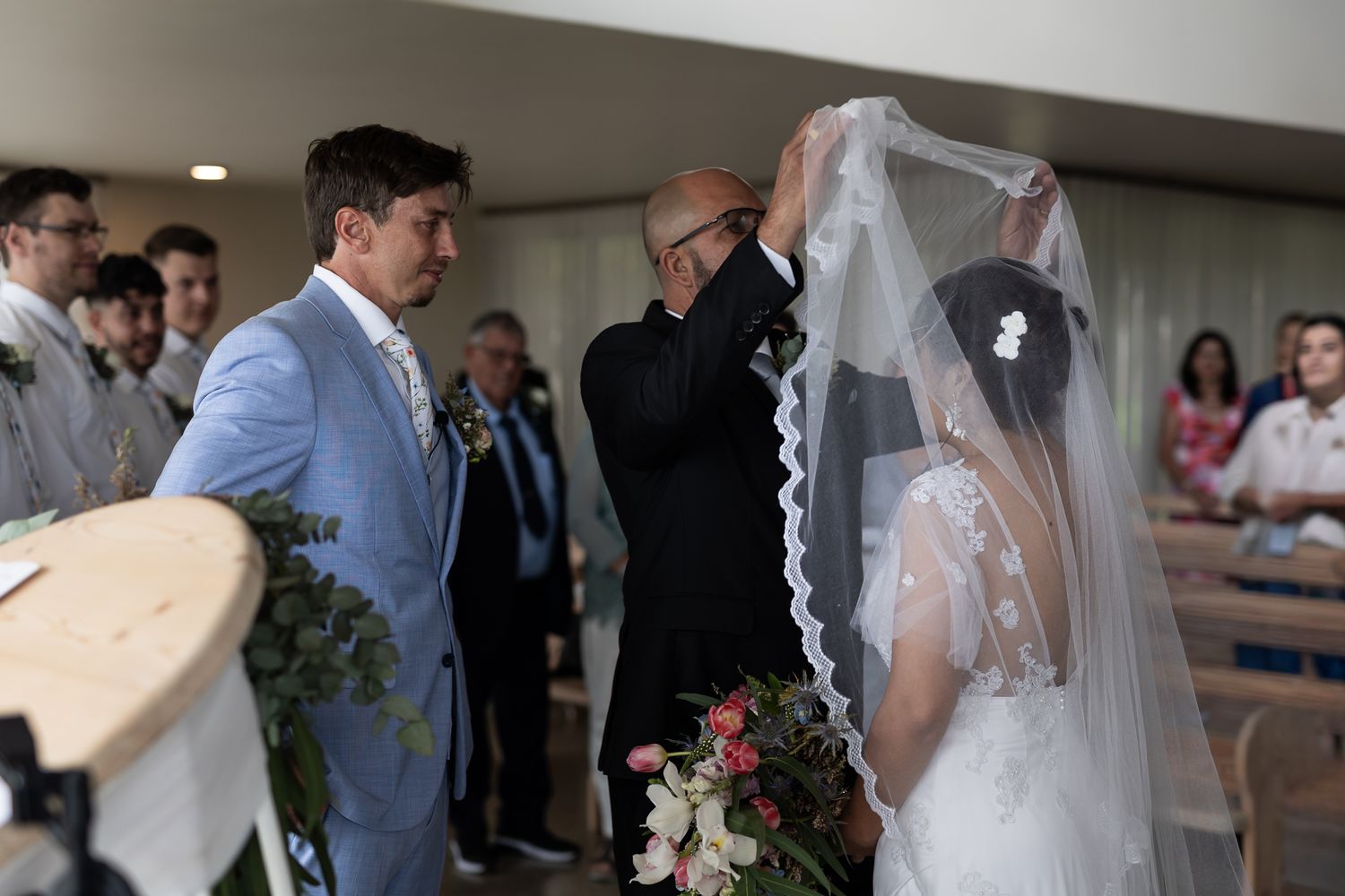 A touching moment as the veil is adjusted during an indoor wedding ceremony.