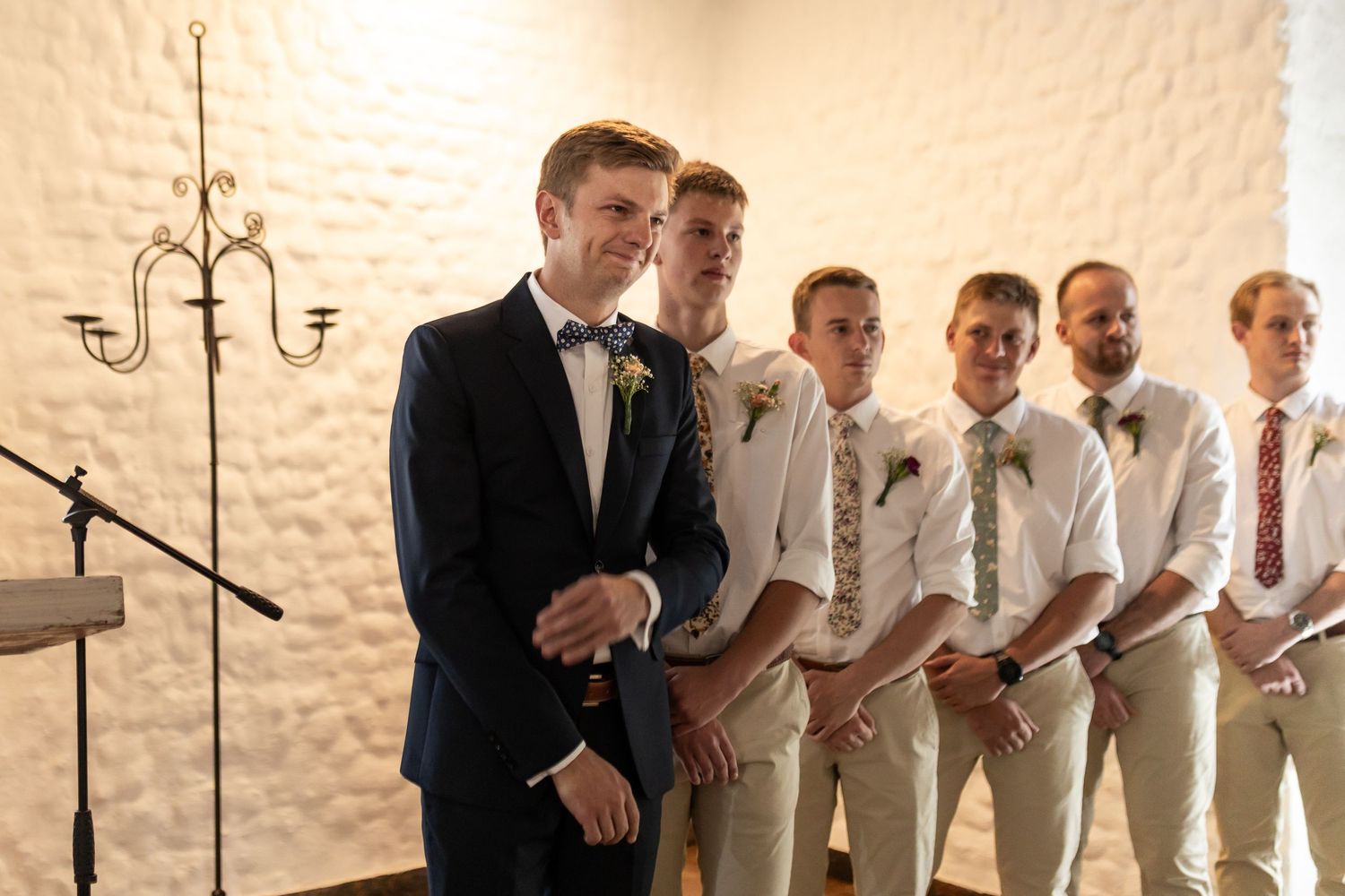 Groomsmen lined up at altar wearing light colored suits with ties during wedding ceremony.