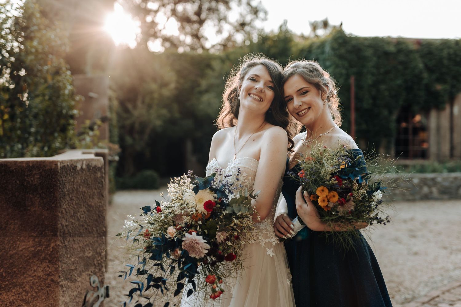 Joyful wedding photo of bride and bridesmaid laughing together in evening sunlight.