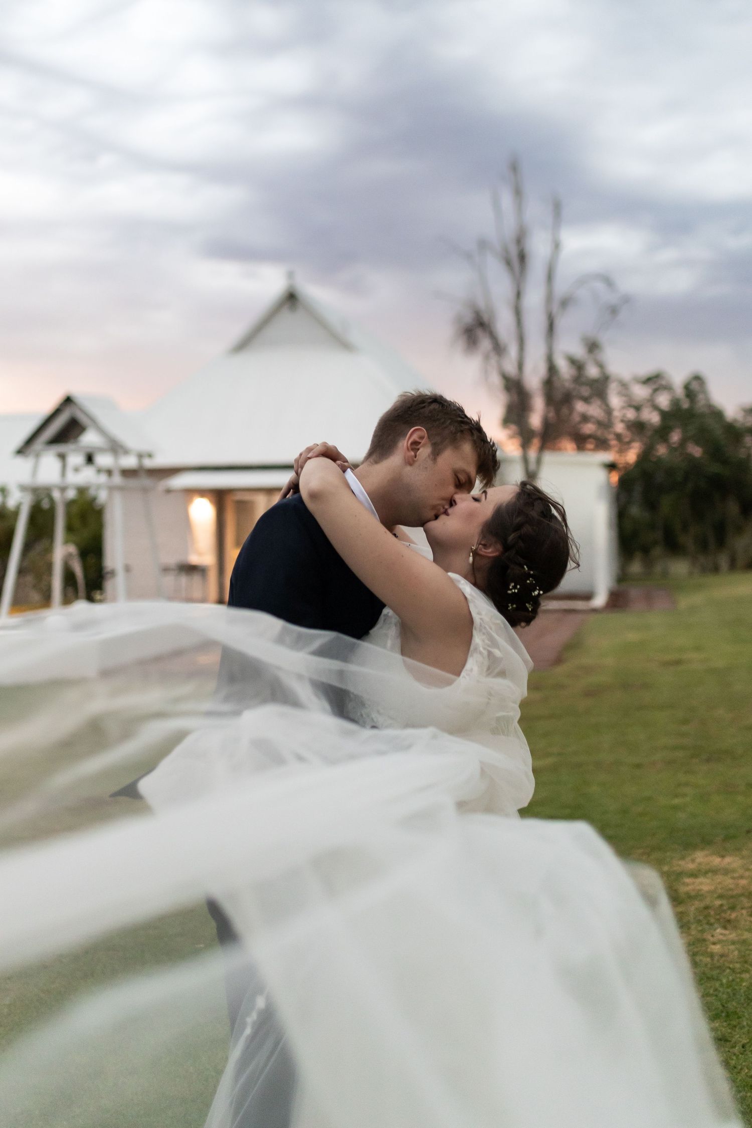 Newlyweds share an intimate dance moment as the bride's veil flows dramatically in the evening light.