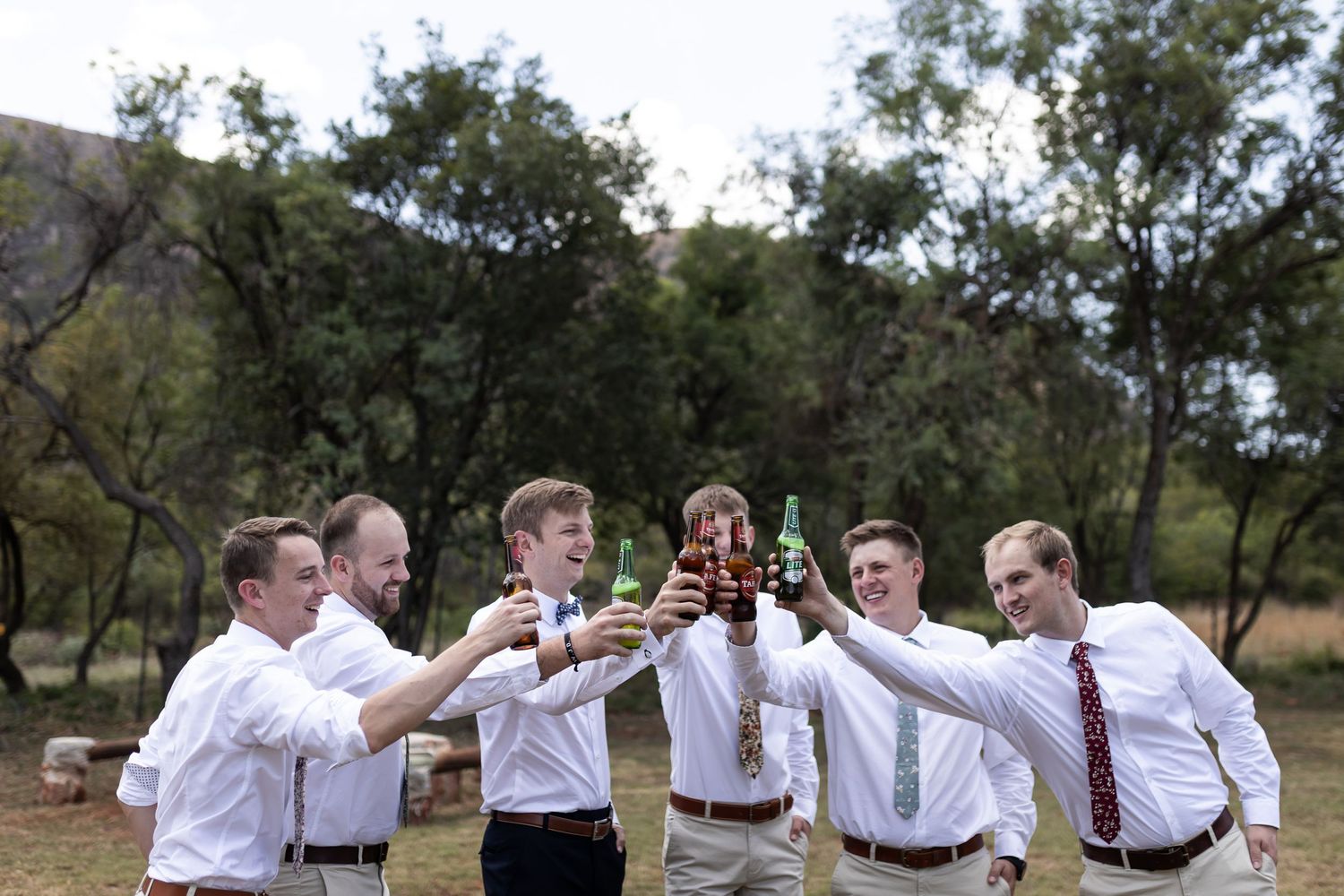 Groomsmen and groom clink bottles together in a circle for a group toast.