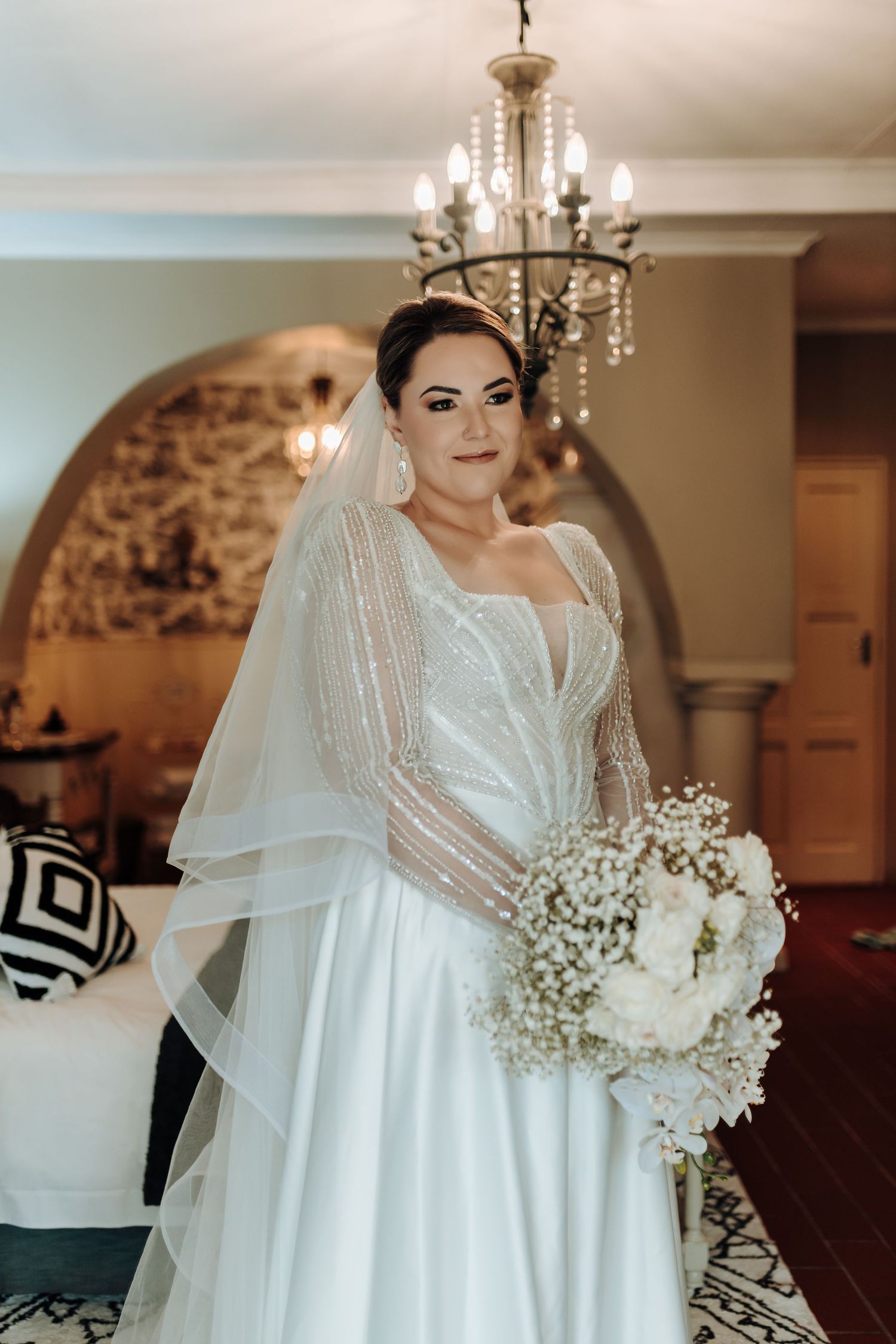 Elegant wedding portrait showcasing detailed sleeve beadwork and dramatic white floral arrangement.