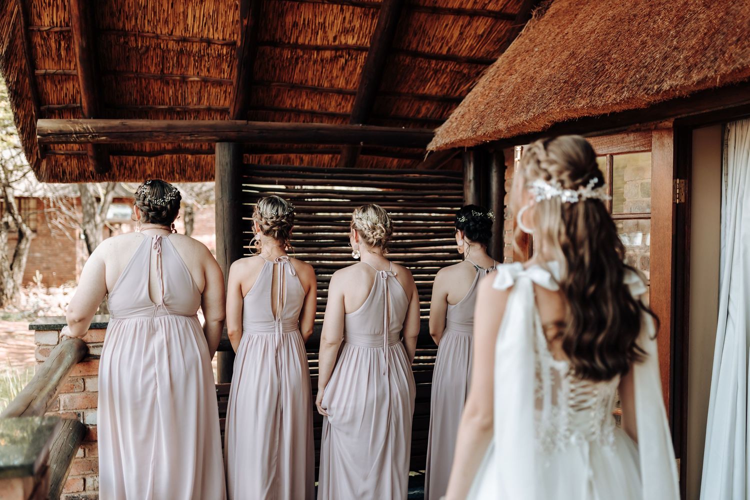 View from behind of attendants in mauve dresses standing on a covered porch.