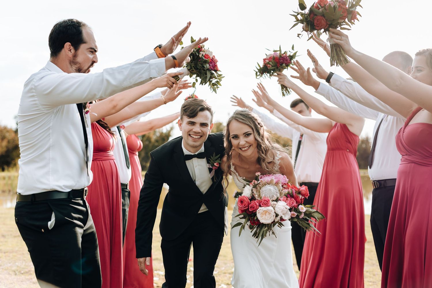 Wedding party jumps and celebrates with raised arms outdoors.