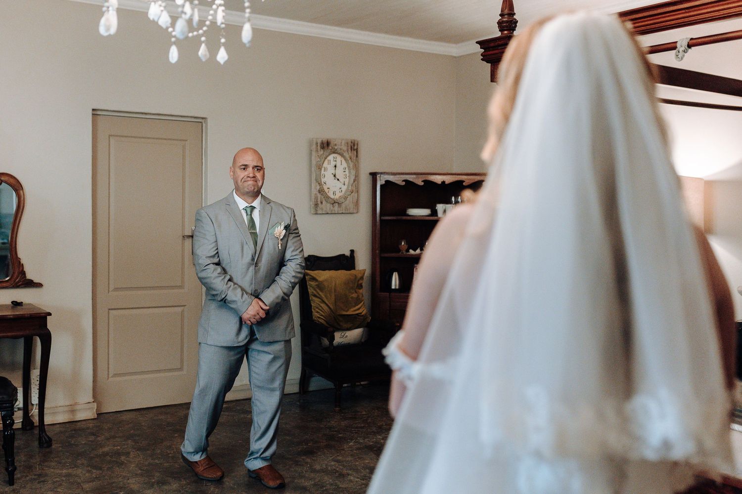 A first look moment captured in an elegant room with a crystal chandelier overhead.