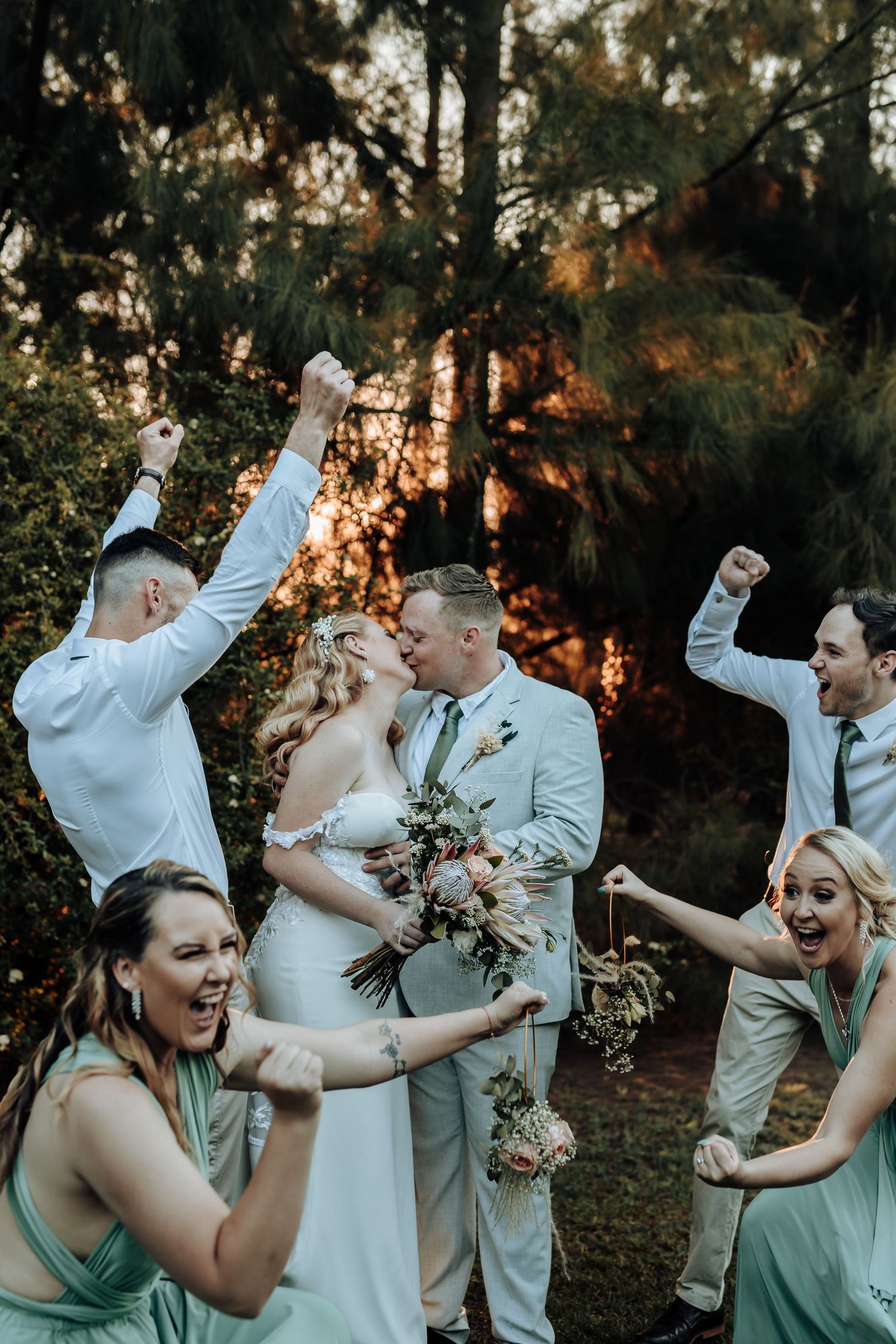 Wedding party celebrating with enthusiastic poses and raised arms in forest setting.
