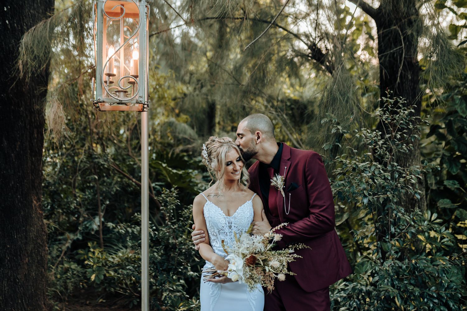 Wedding couple poses by a decorative lantern in a lush garden setting.
