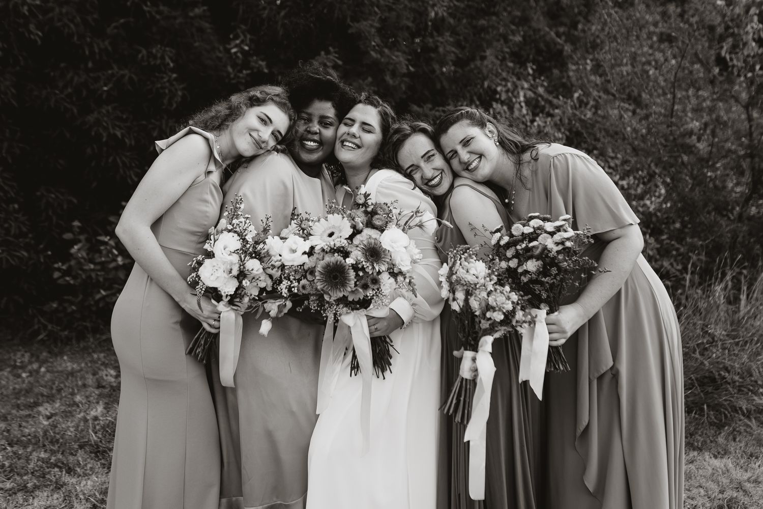 Black and white photo of bridal party huddled together smiling with bouquets.