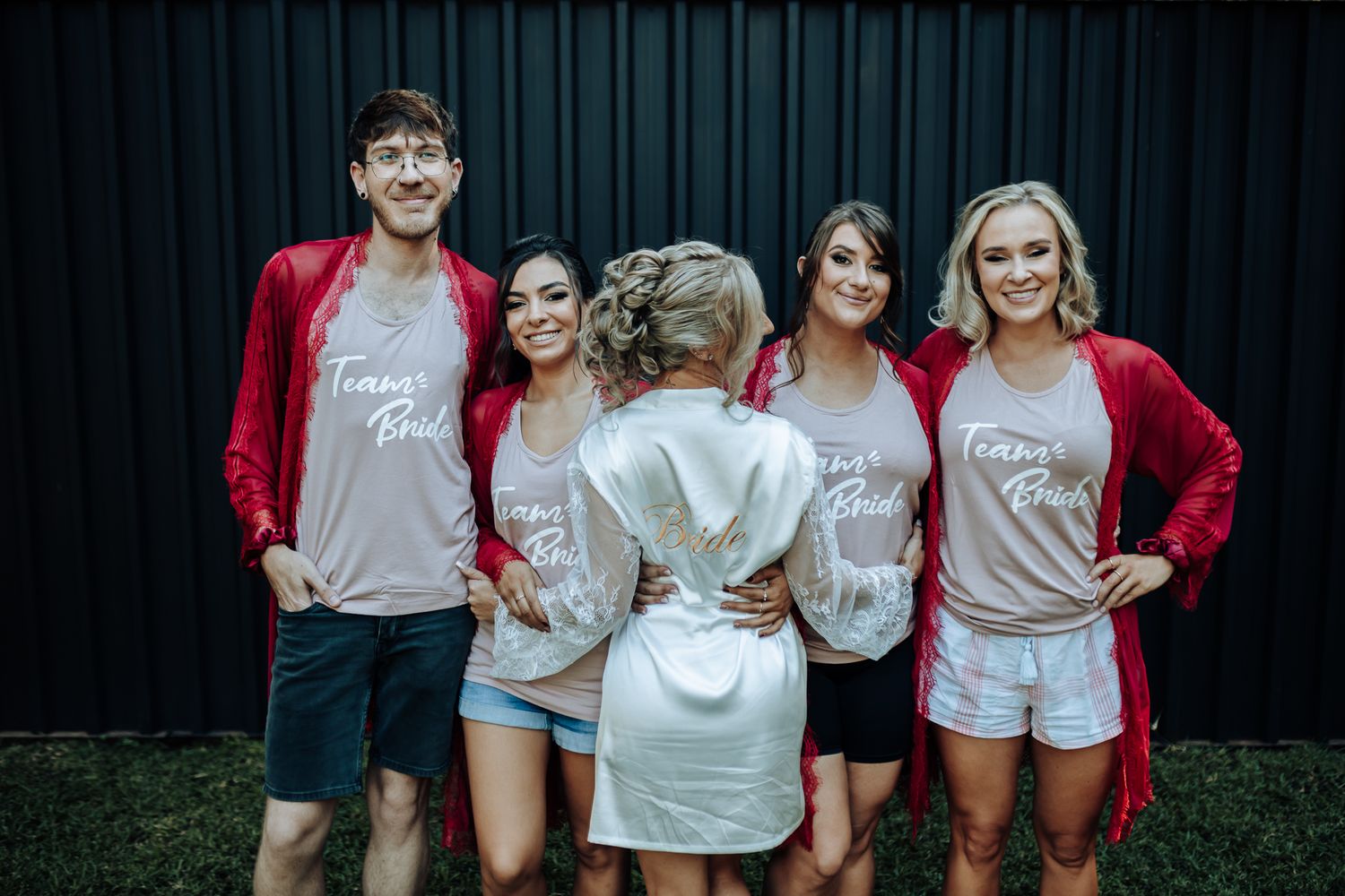 Wedding party wearing matching gray t-shirts and red cardigans poses together before the ceremony.
