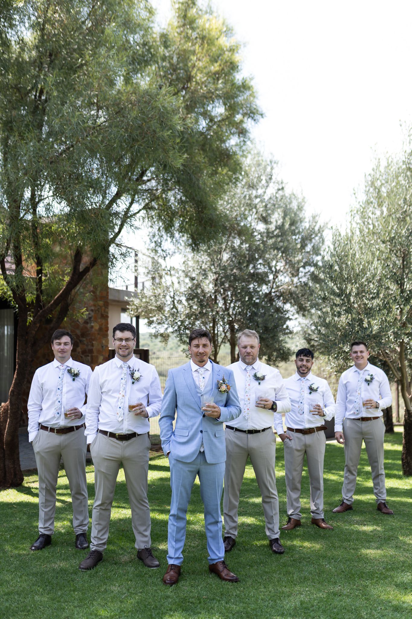 Groomsmen in coordinated attire pose on green lawn with central figure in light blue suit.
