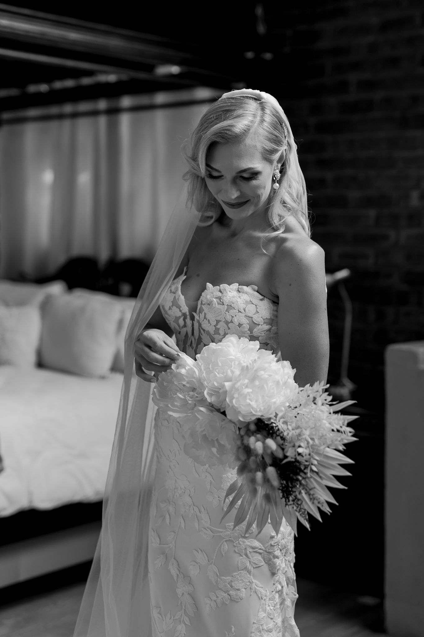 Black and white close-up of bride holding white floral bouquet in lace detailed dress.