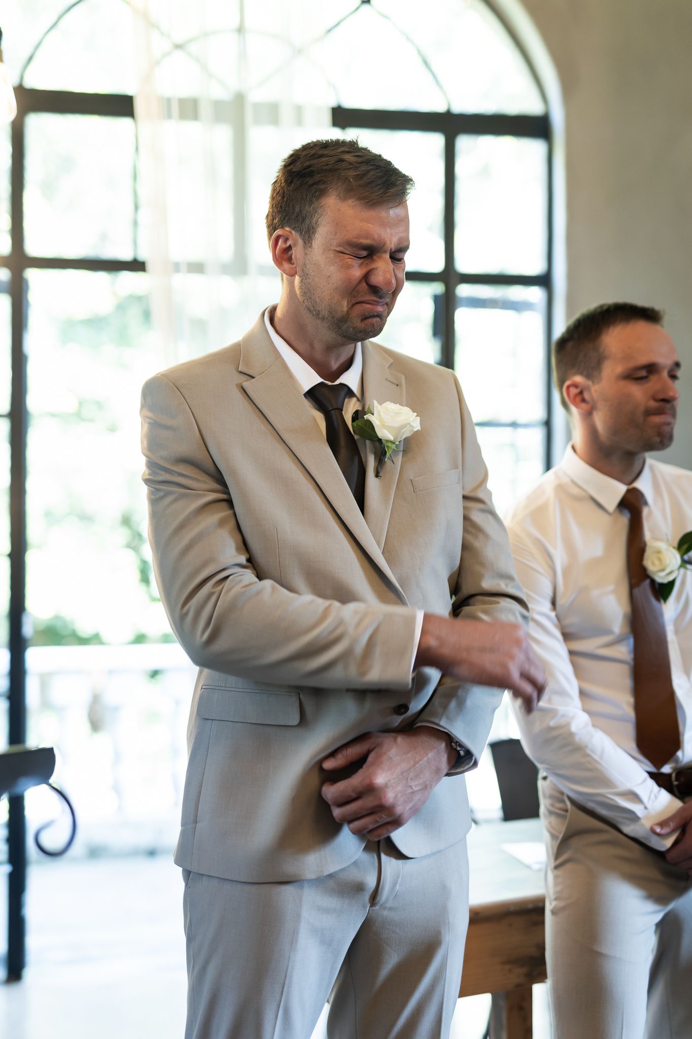 Wedding party members in light suits and boutonnieres prepare for ceremony in elegant venue.